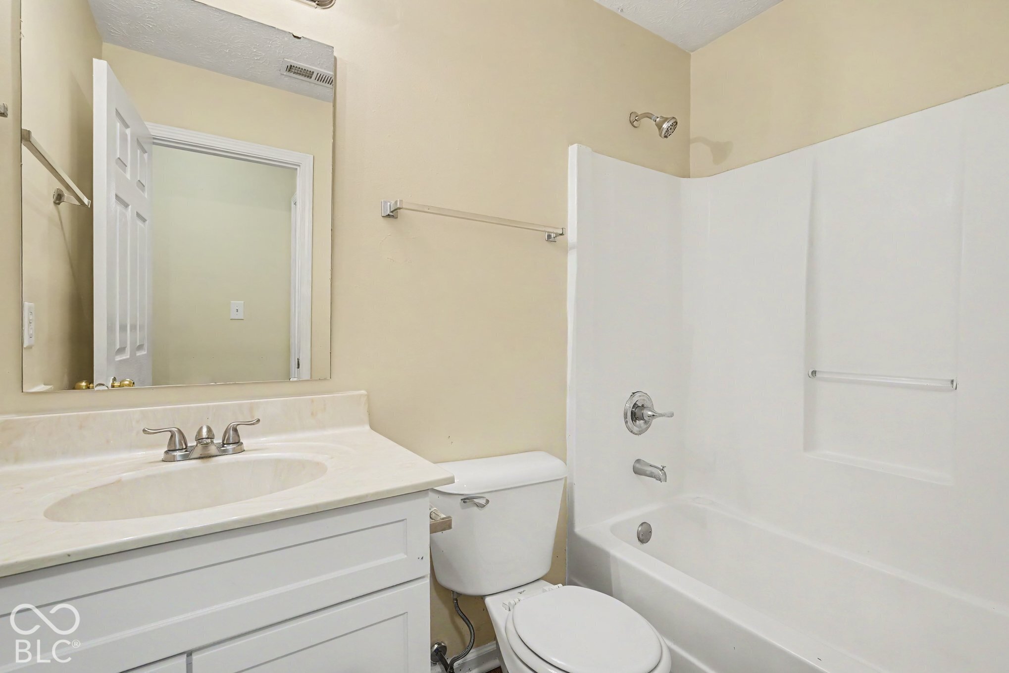 White vanity cabinet with an integrated sink, solid-surface countertop, chrome dual-handle faucet, large vanity mirror, and a white acrylic tub-shower combination