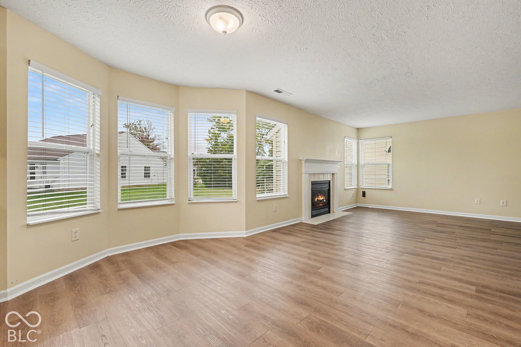 Spacious room featuring wood-finish flooring, a bay window configuration, and a fireplace with a mantel