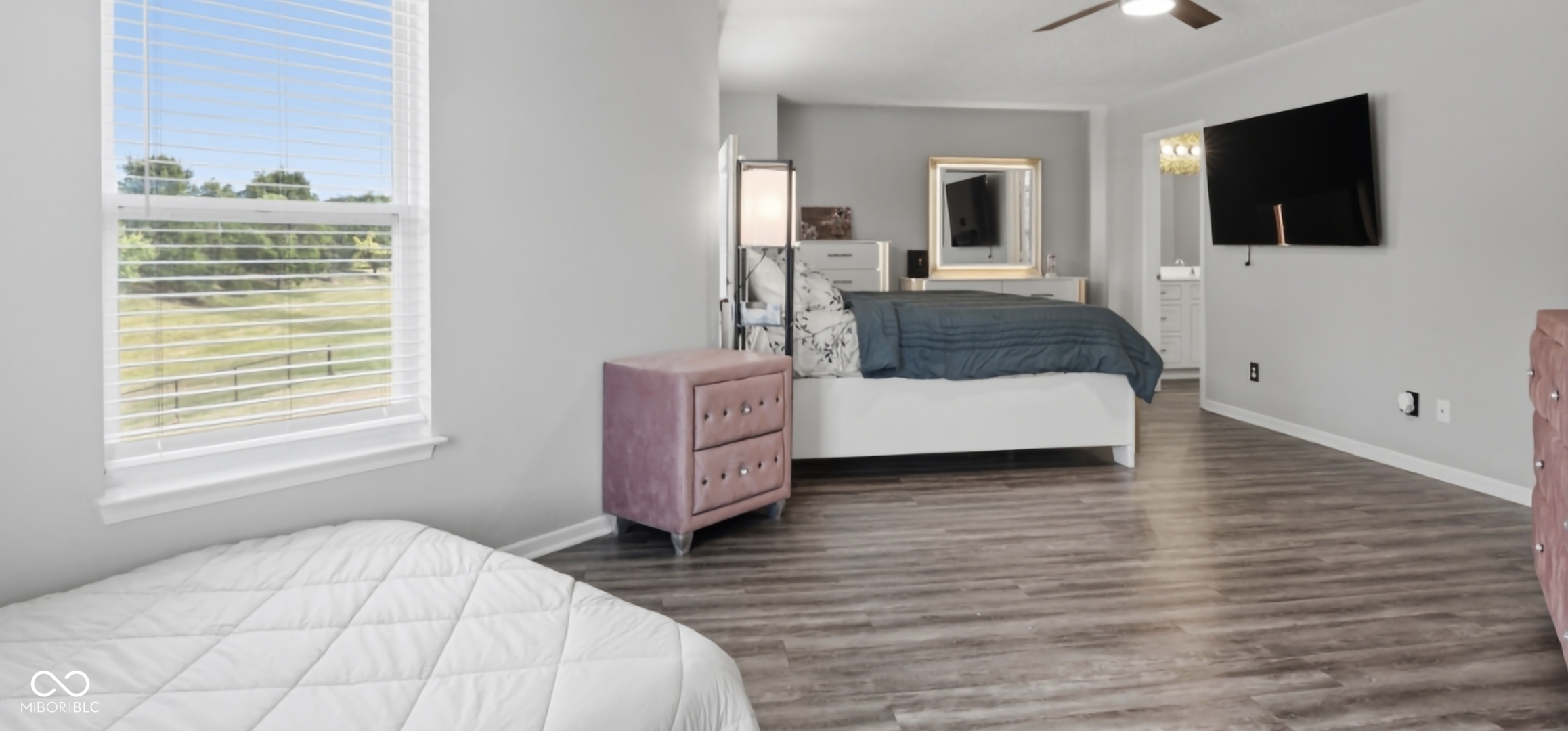 Spacious room featuring wood-finish flooring, a ceiling fan, and a large window with horizontal blinds
