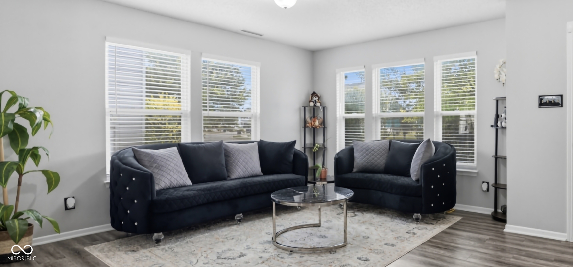 Living area featuring light gray walls, wood-finish flooring, white window blinds, and a built-in overhead light fixture