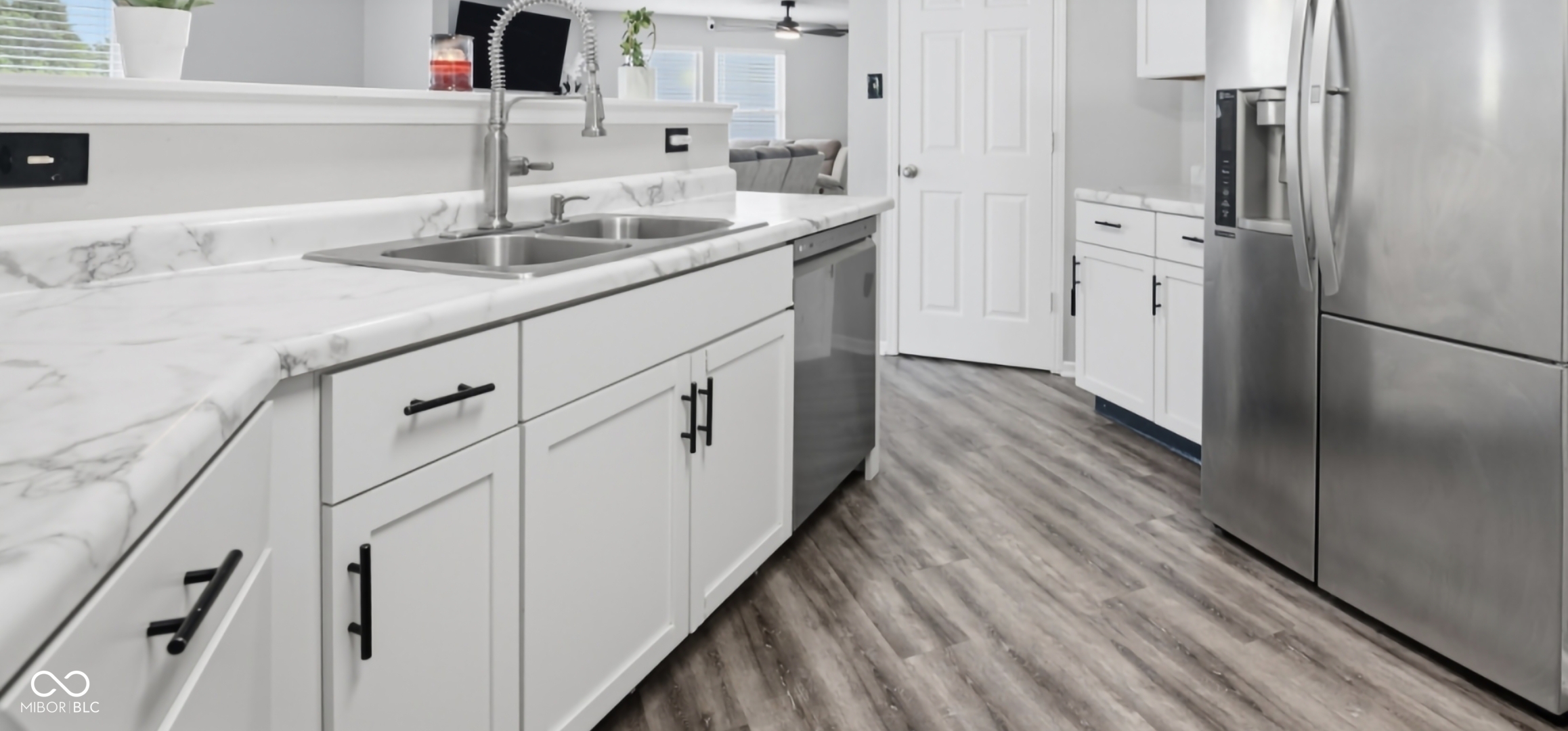 Kitchen featuring wood-finish flooring, white cabinetry with matte black hardware, and a double basin stainless steel sink with a gooseneck faucet