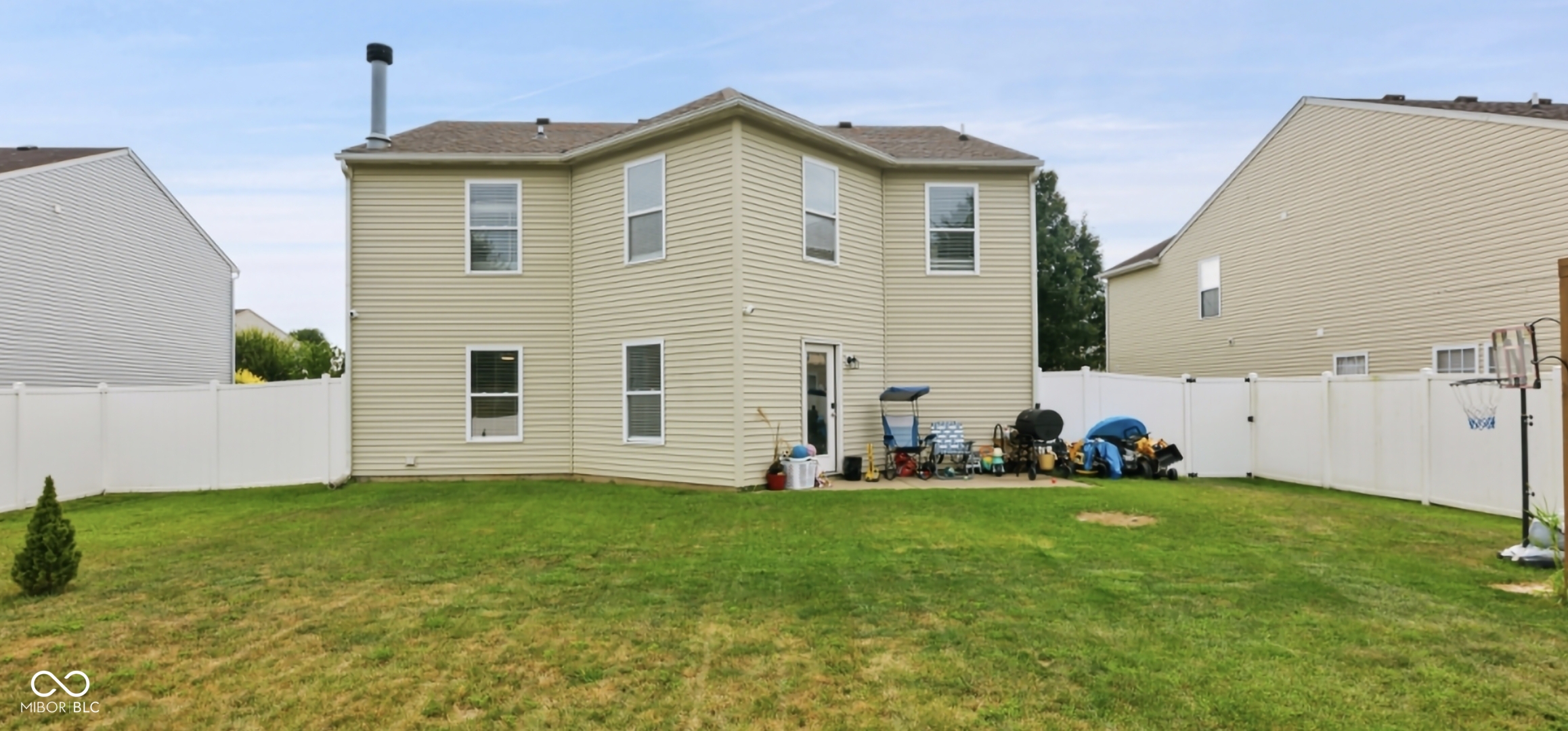Rear exterior featuring light-colored siding, multiple windows, a ground-level patio, and a white privacy fence encompassing the yard