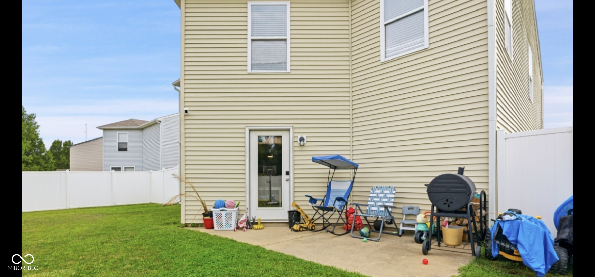Expansive backyard featuring a manicured lawn, a concrete patio, and a white privacy fence