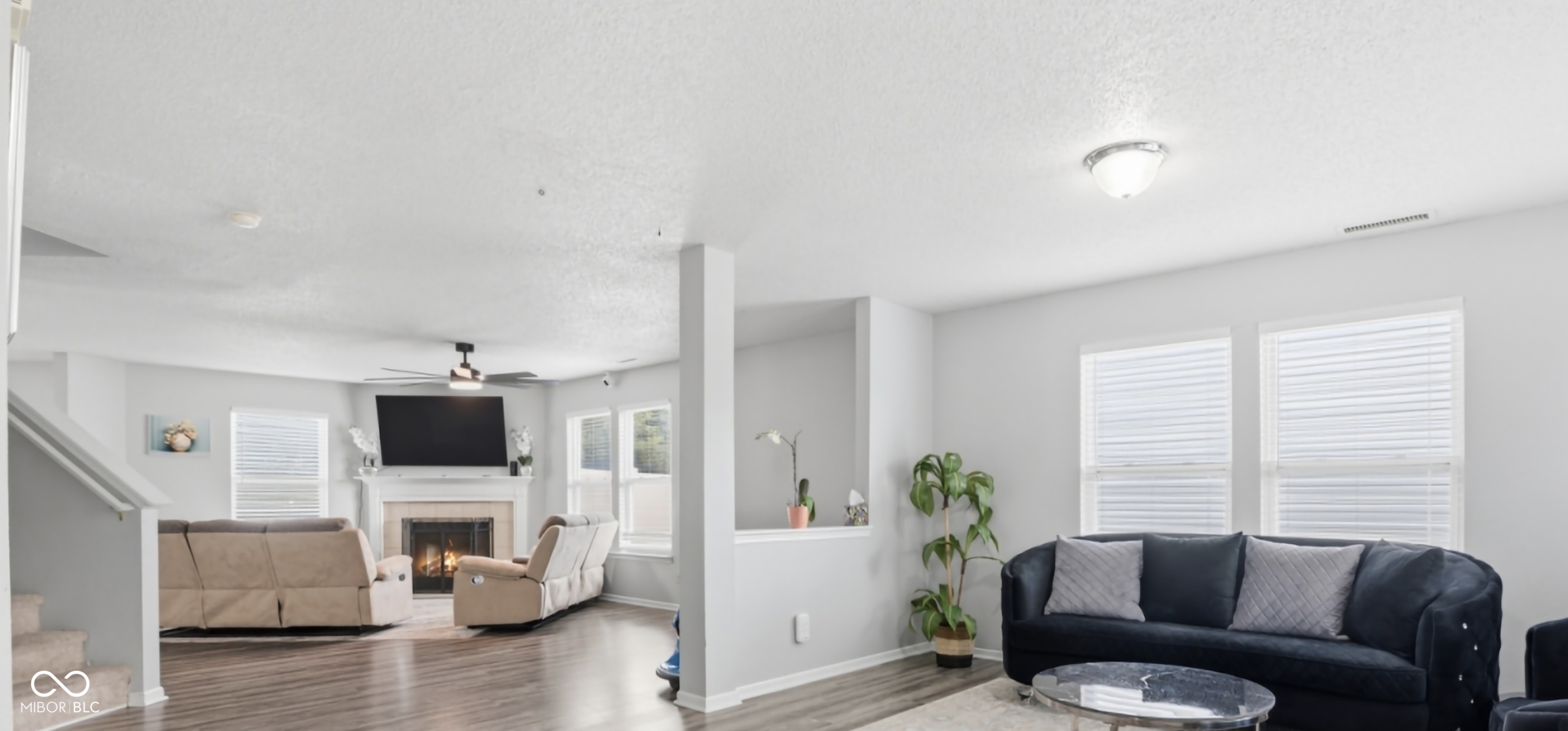Spacious living area featuring wood-finish flooring, a fireplace with a mantel, multiple windows with blinds, and a ceiling fan