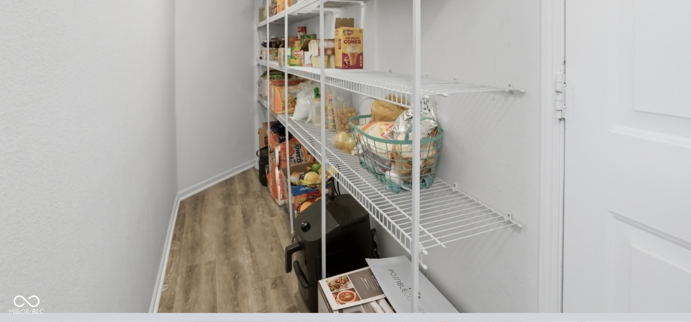 Walk-in pantry featuring extensive wire shelving, wood-finish flooring, and white baseboards