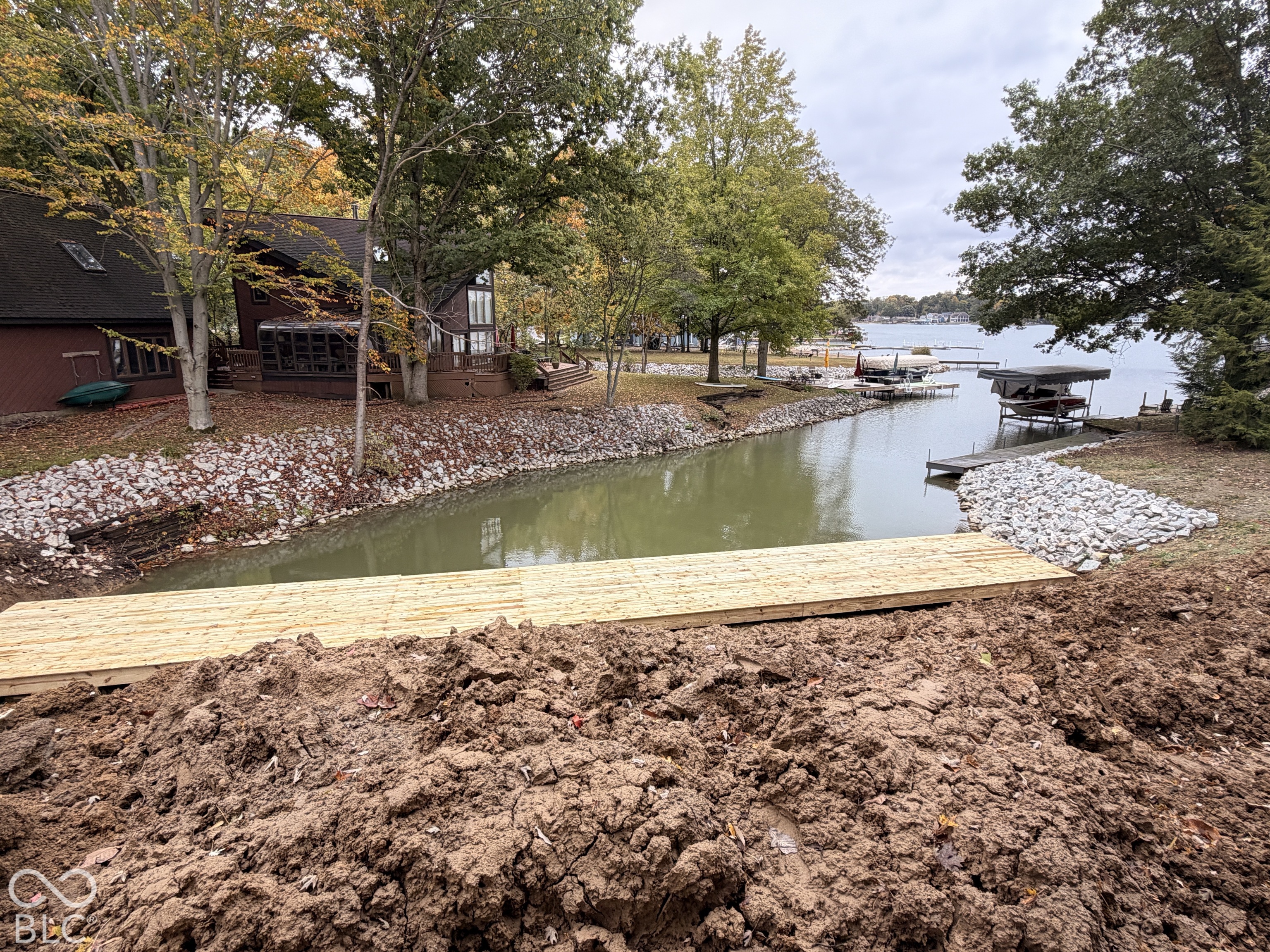 Waterfront property featuring a wood dock, stone shoreline stabilization, and mature trees