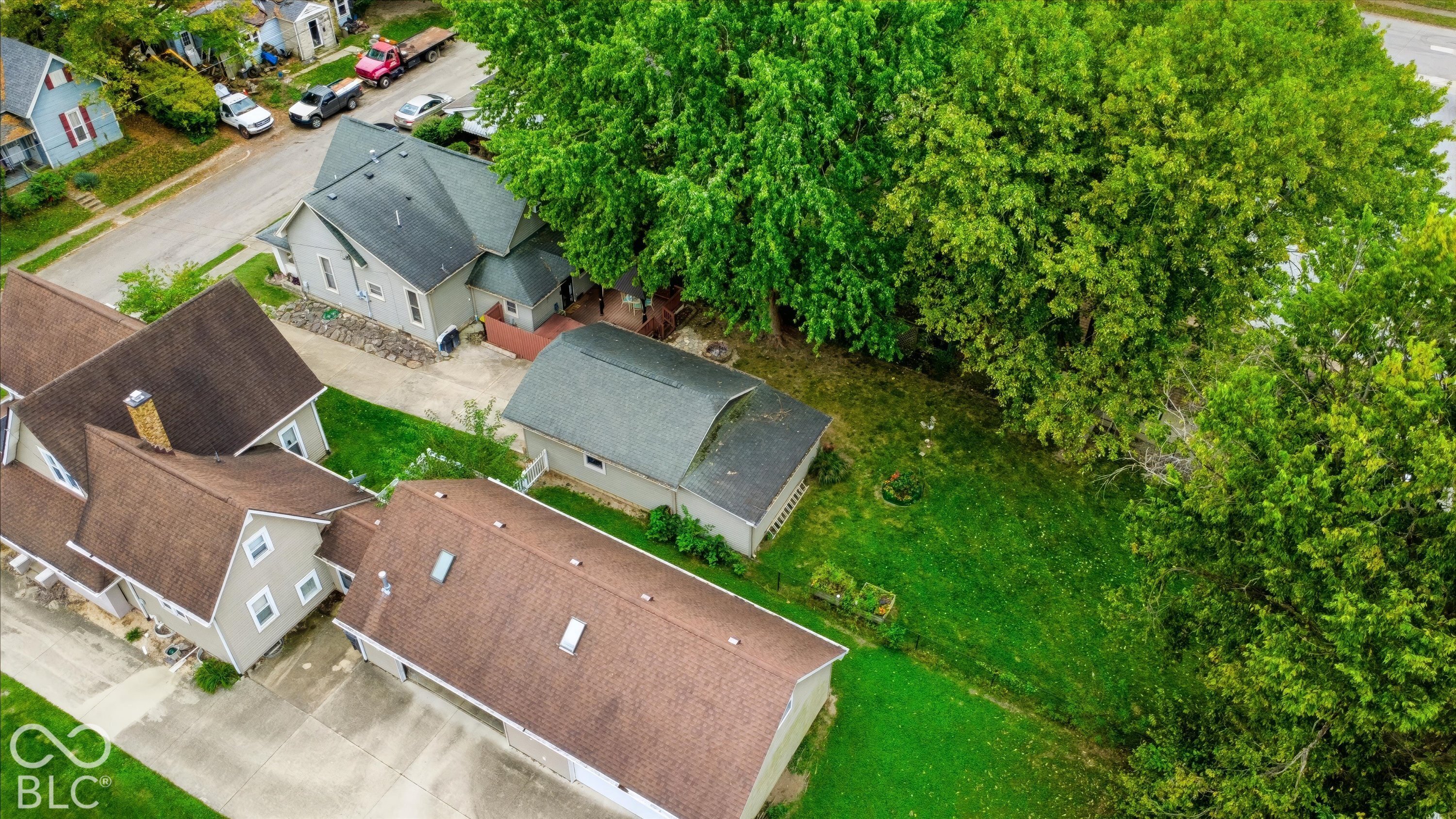 Aerial perspective featuring a detached multi-car garage, concrete driveway, and expansive rear lawn with mature trees