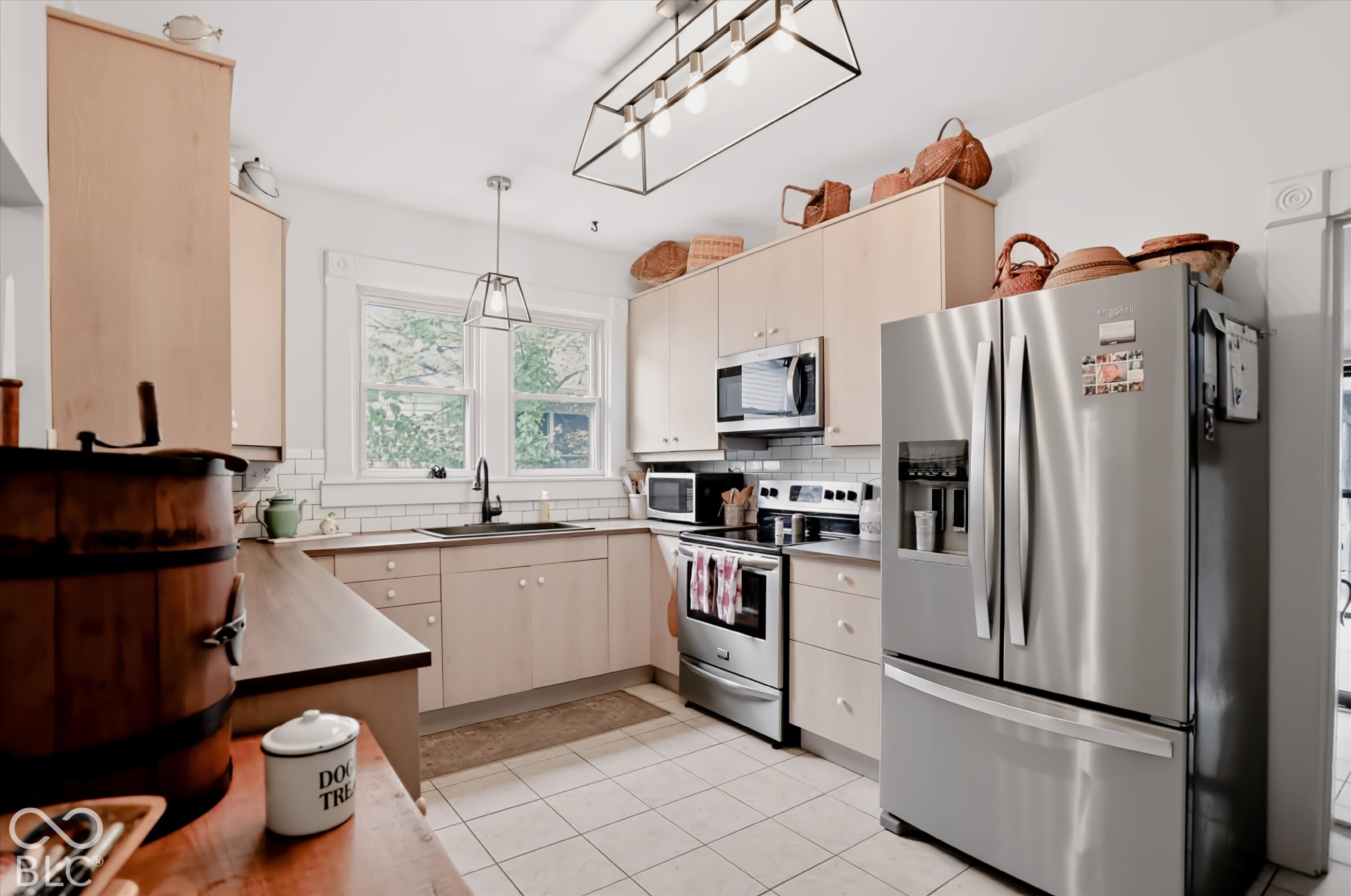 Kitchen featuring light-finish cabinetry, stainless steel appliances, white subway tile backsplash, matte black faucet, and geometric pendant lighting