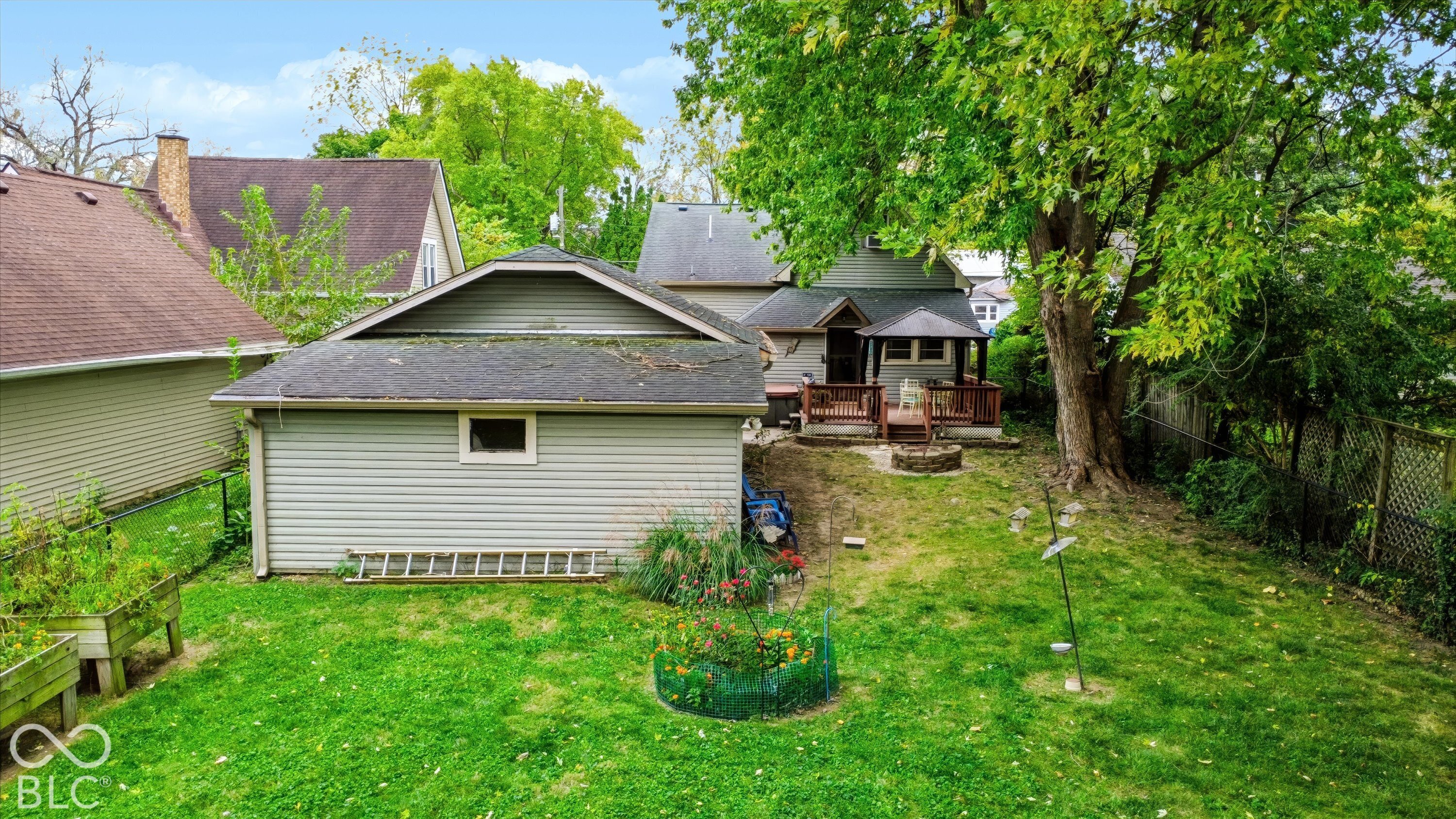 Backyard featuring a detached garage, a wooden deck, a stone fire pit, and mature trees