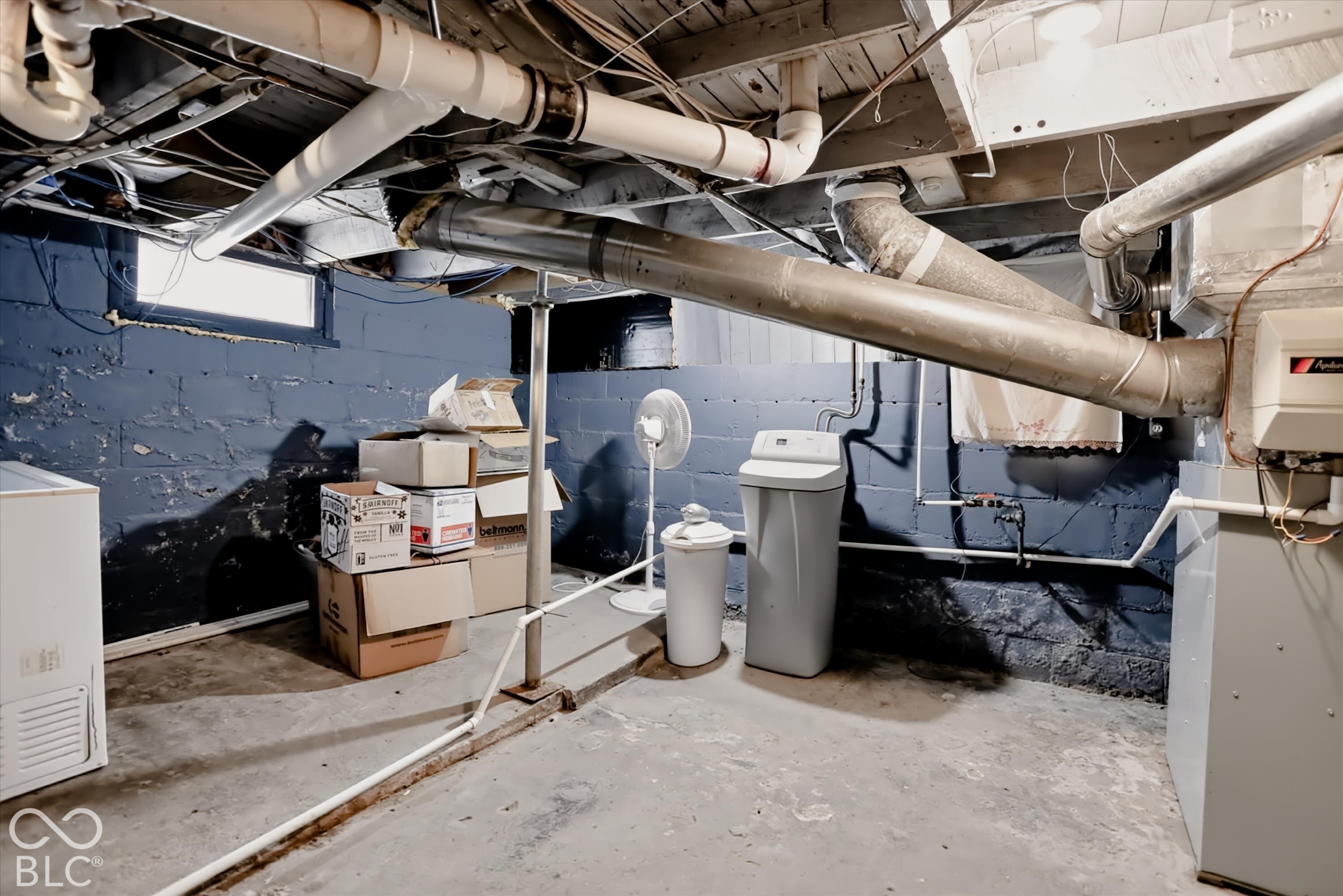 Unfinished basement featuring concrete foundation walls, exposed ceiling joists, concrete flooring, and an installed water softener system