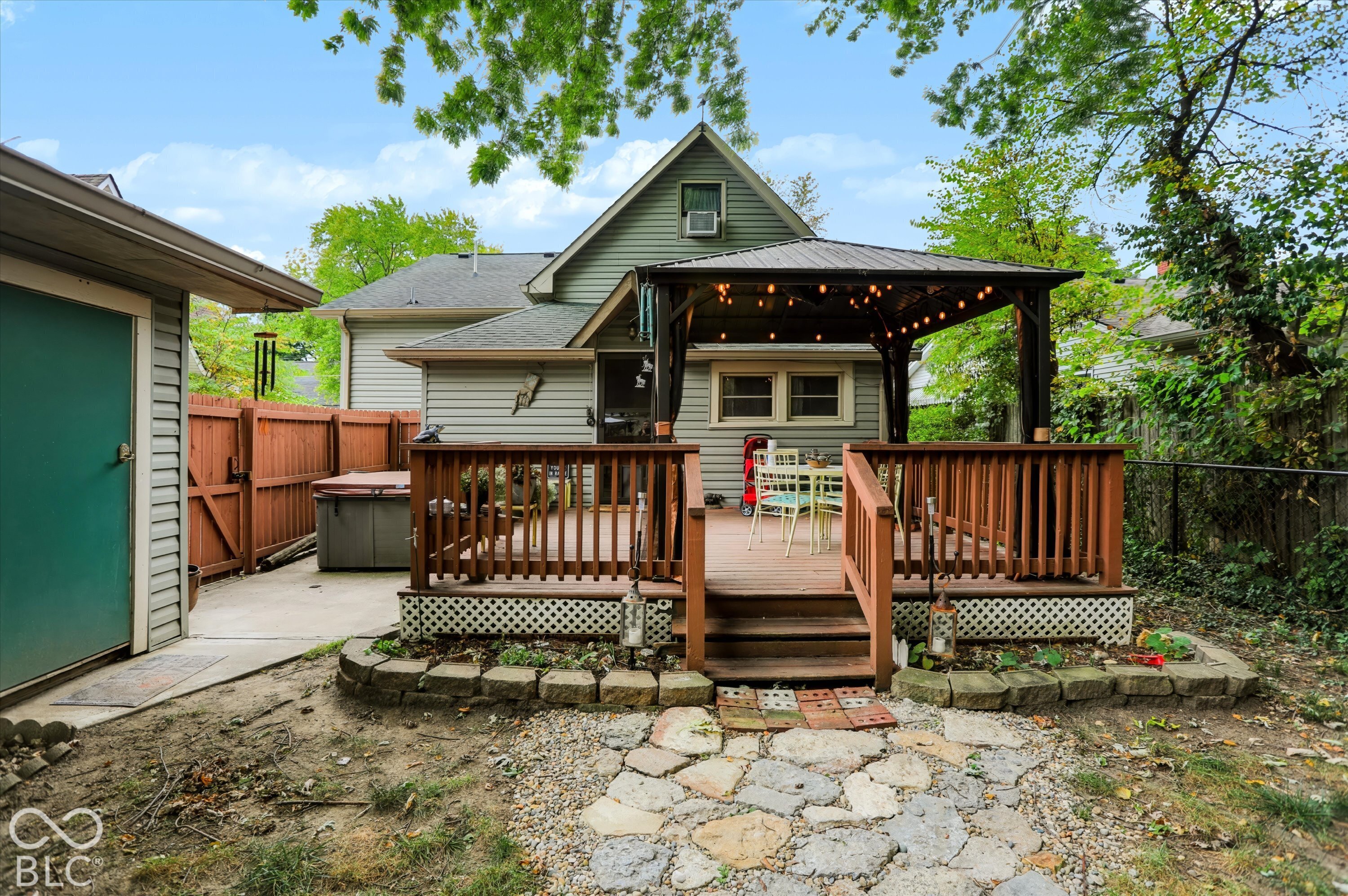 Elevated wooden deck with integrated gazebo structure, concrete patio area, stone-style hardscaping, and wood privacy fencing
