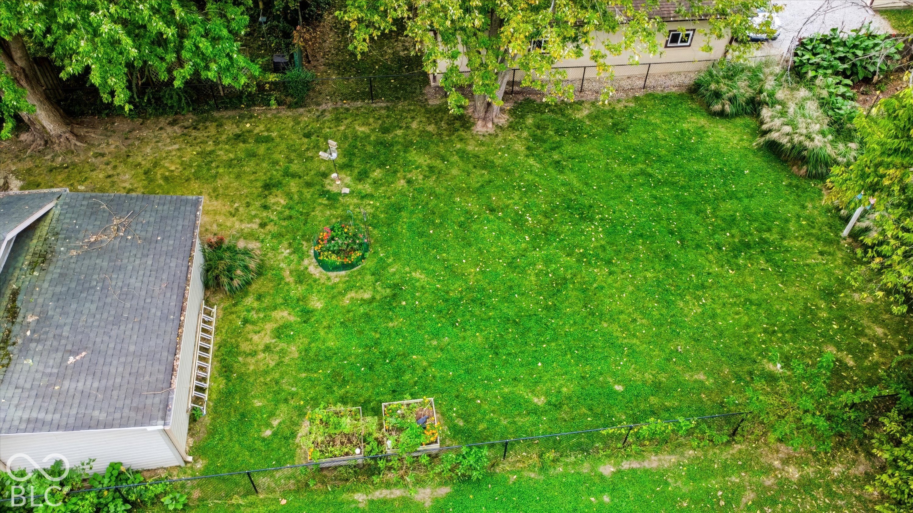 Fenced backyard featuring a manicured lawn, established shade trees, perimeter fencing, and raised planting beds