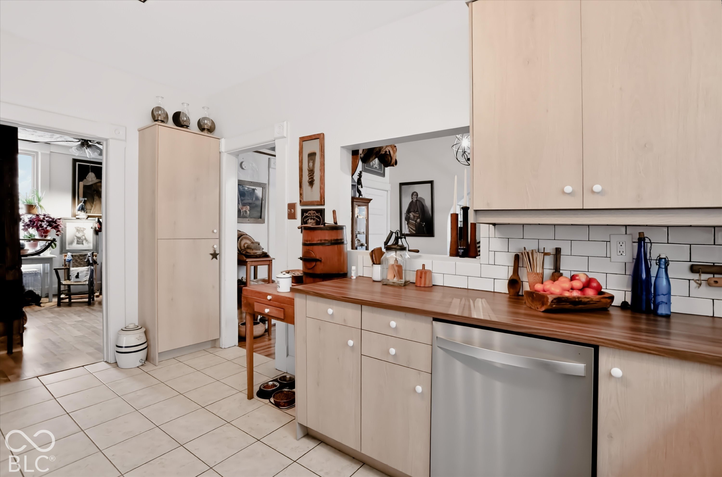 Light wood-finish cabinetry featuring a pass-through window, butcher block countertop, white subway tile backsplash, and stainless steel dishwasher