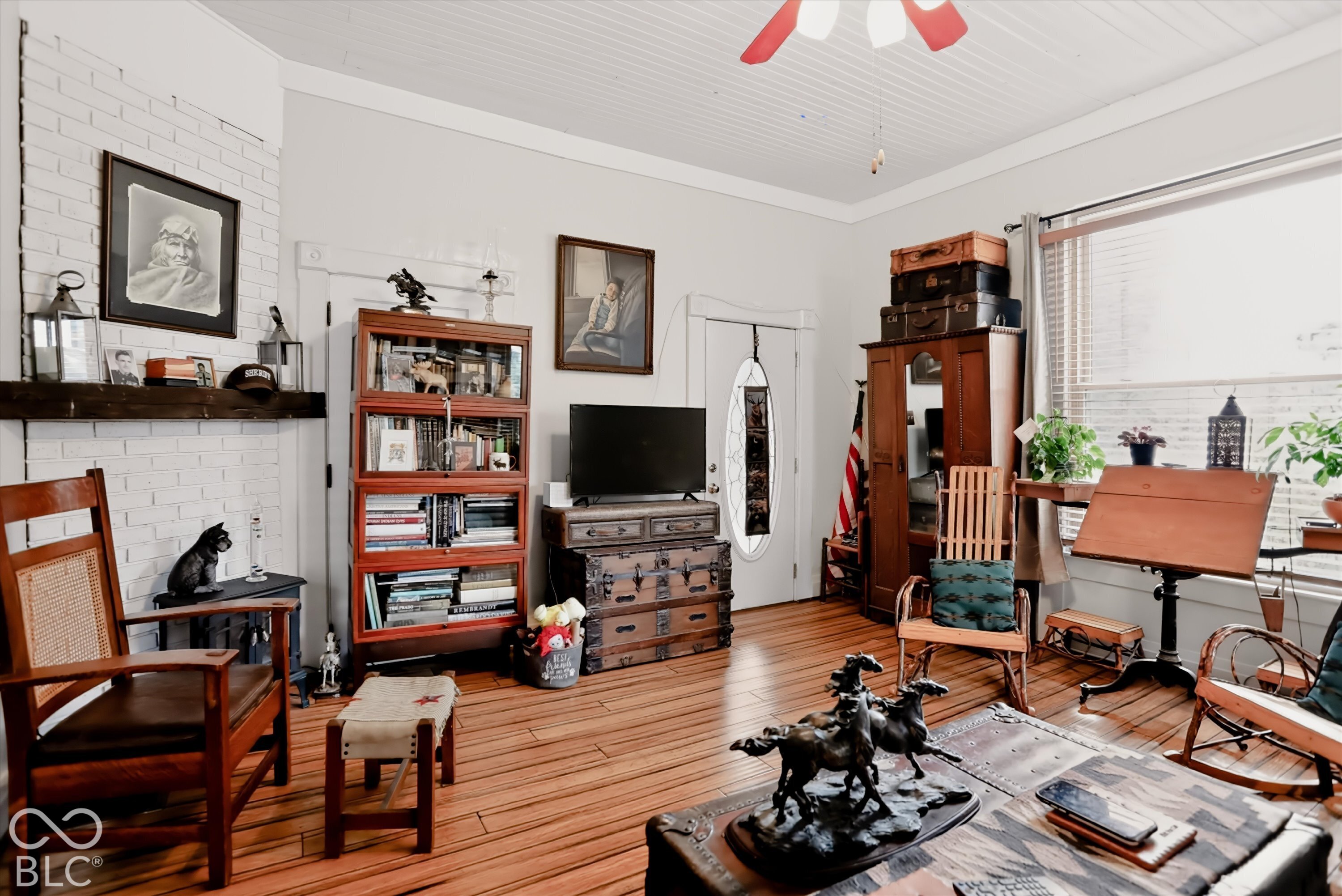 Painted brick fireplace with a dark timber mantel, beadboard ceiling, wood-finish flooring, and a glass-paneled entry door