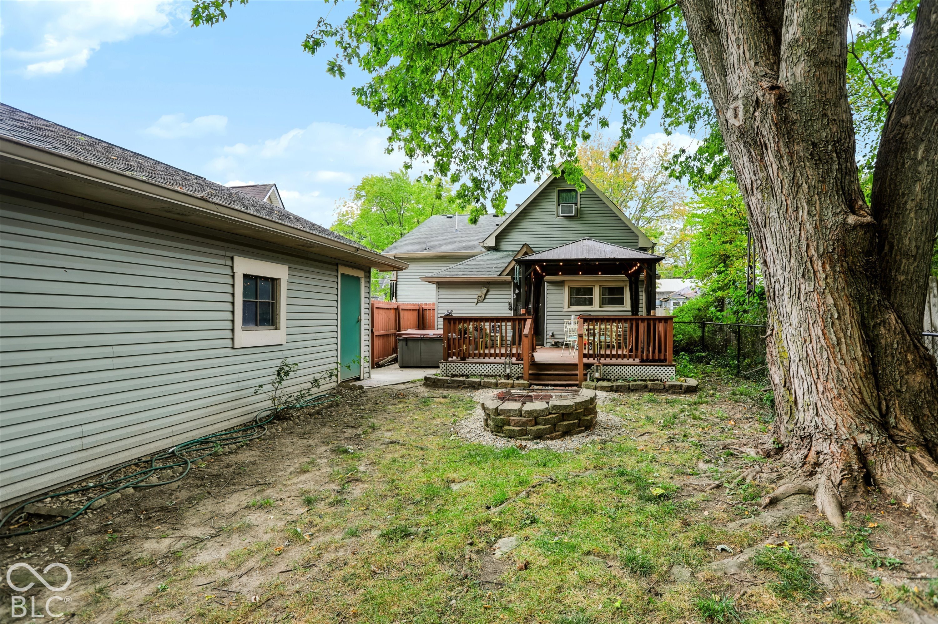 Backyard featuring a raised wooden deck with a built-in pergola, a circular stone fire pit, and a mature tree