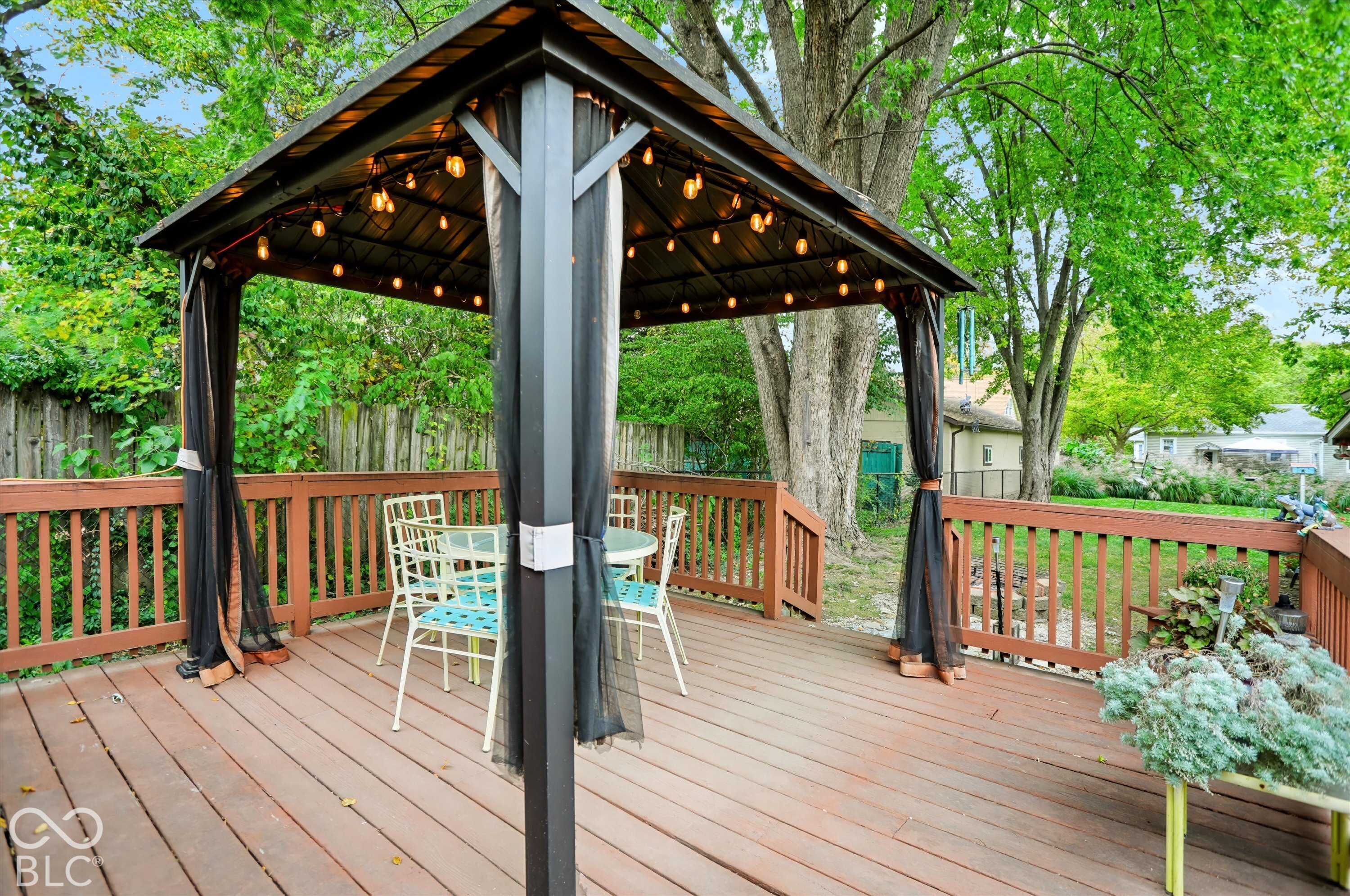 Elevated wood deck featuring a metal-framed gazebo with a permanent canopy and integrated string lighting, enclosed by a wood railing