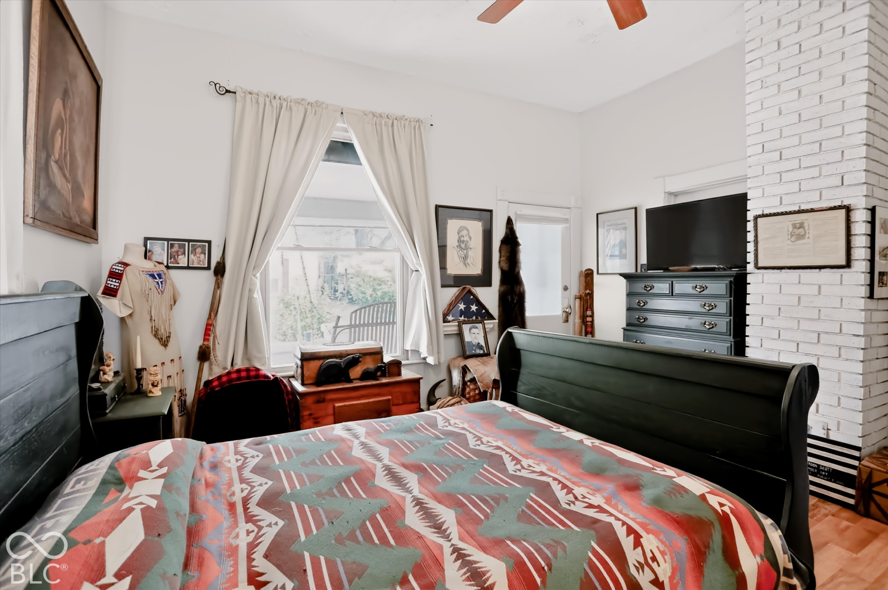 Painted white brick fireplace chimney, ceiling fan with wood-finish blades, and window with natural light