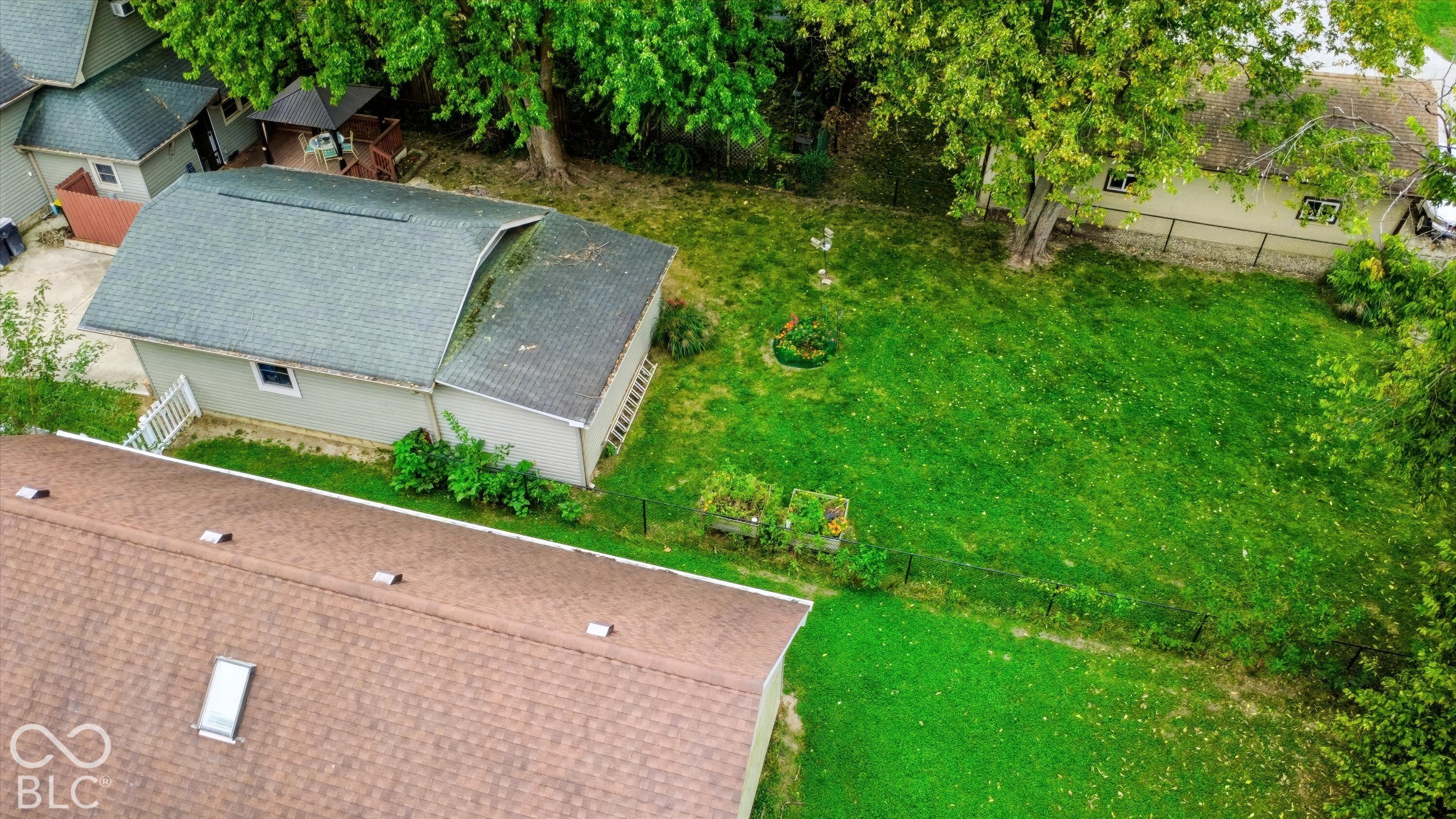 Expansive backyard featuring a grass lawn, mature trees, a detached garage with asphalt shingle roofing, and a wooden gazebo