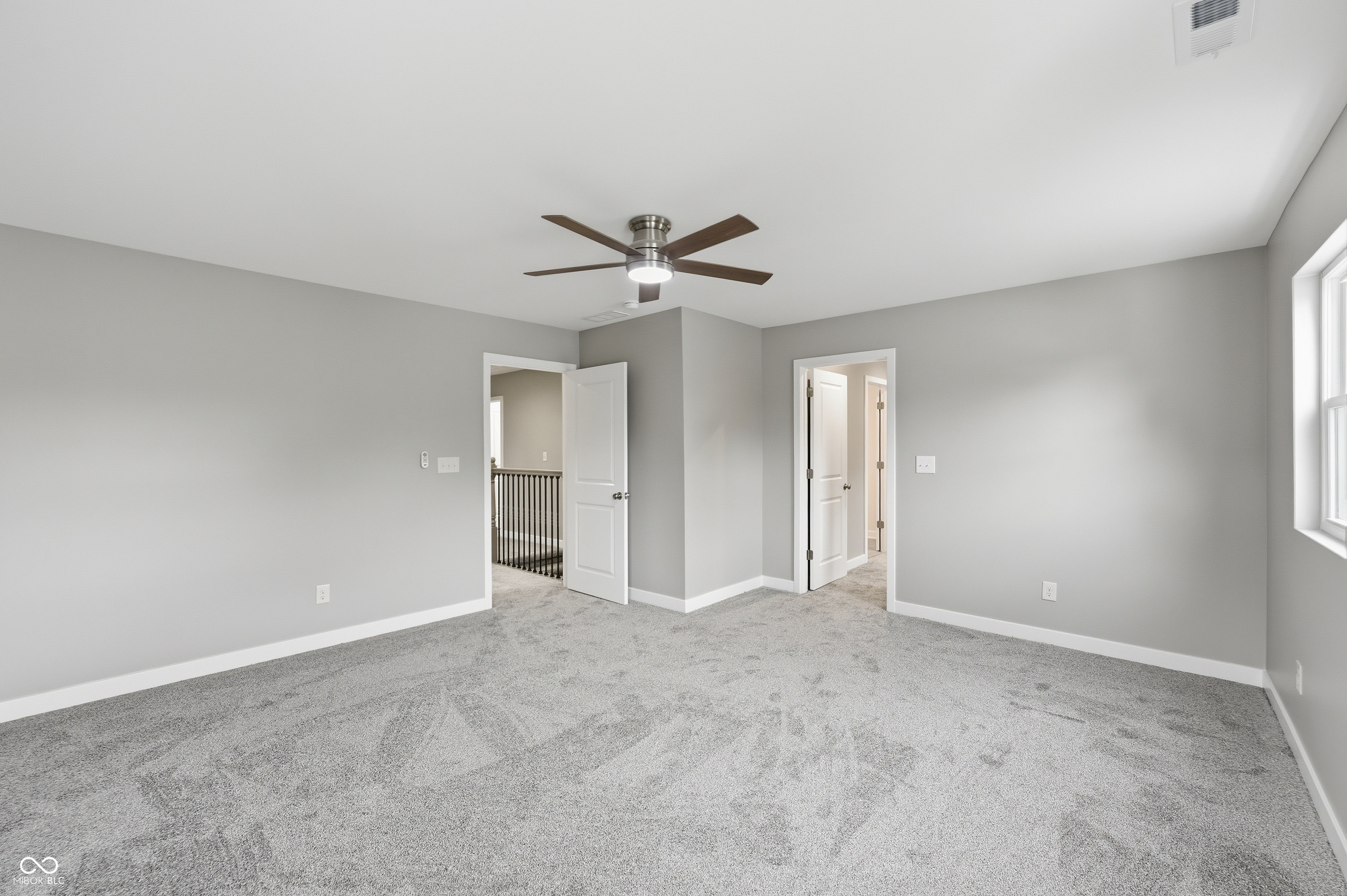 Spacious room featuring neutral grey wall paint, grey carpeting, a ceiling fan with integrated lighting, and white baseboards