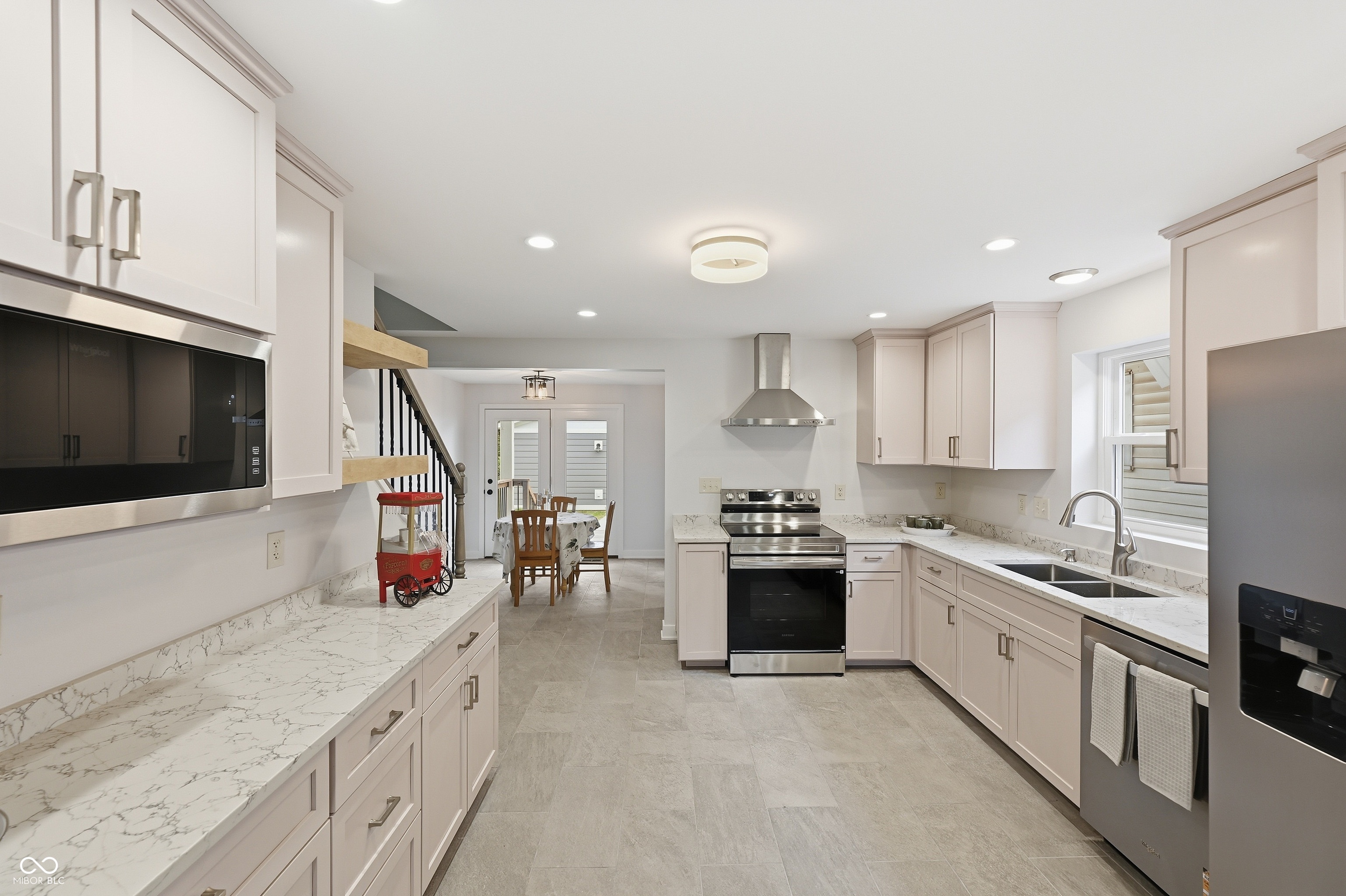 Contemporary kitchen featuring light cabinetry with brushed nickel hardware, white stone countertops, stainless steel appliances, and wood-finish flooring