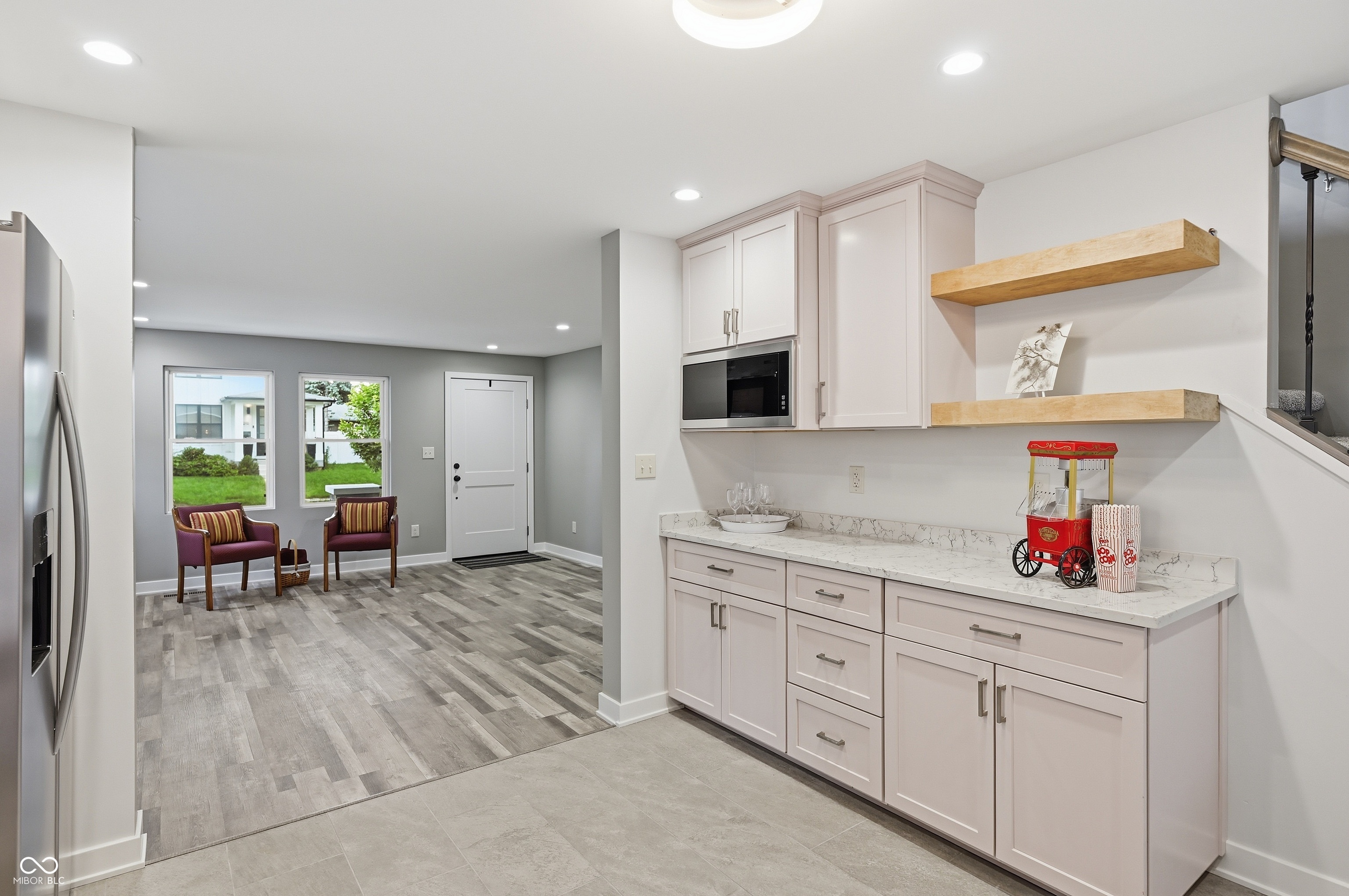 Integrated wet bar with solid surface countertop, light cabinetry, built-in microwave, and open wood shelving