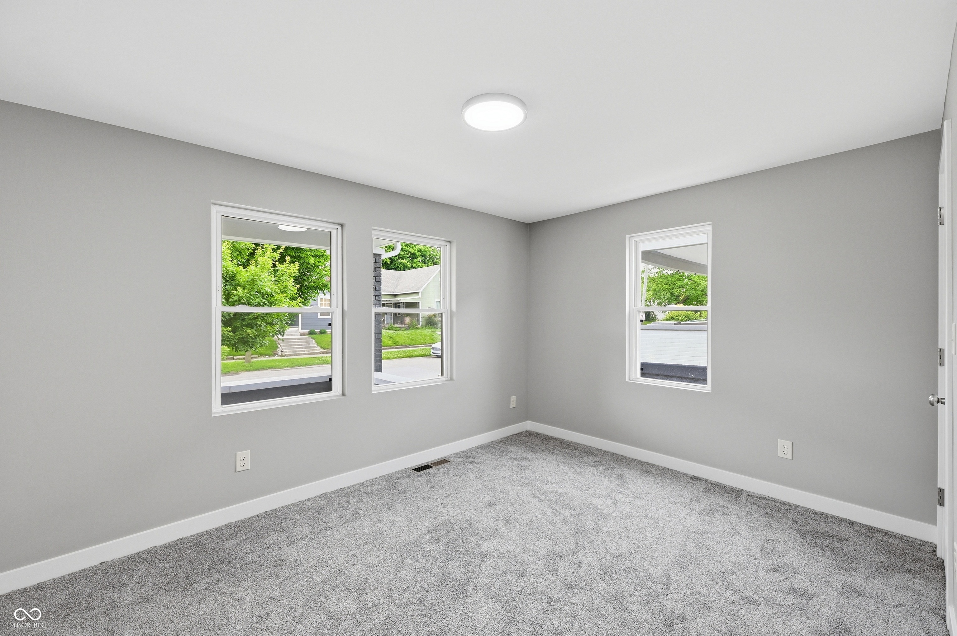 Well-lit room featuring multiple windows, neutral gray walls, plush gray carpeting, white trim, and a ceiling-mounted light fixture