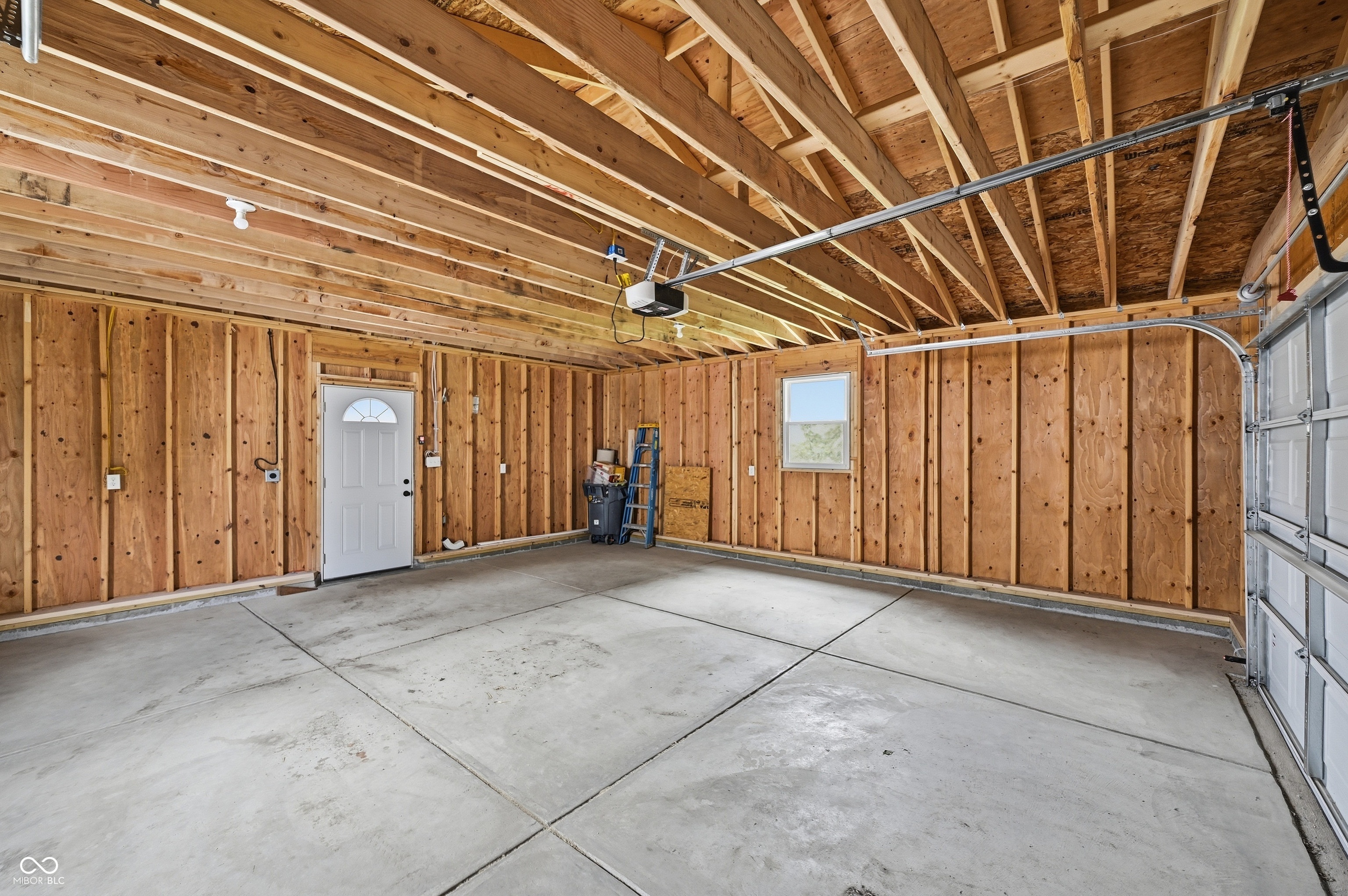 Spacious garage featuring a concrete floor, exposed wood framing, and an overhead garage door