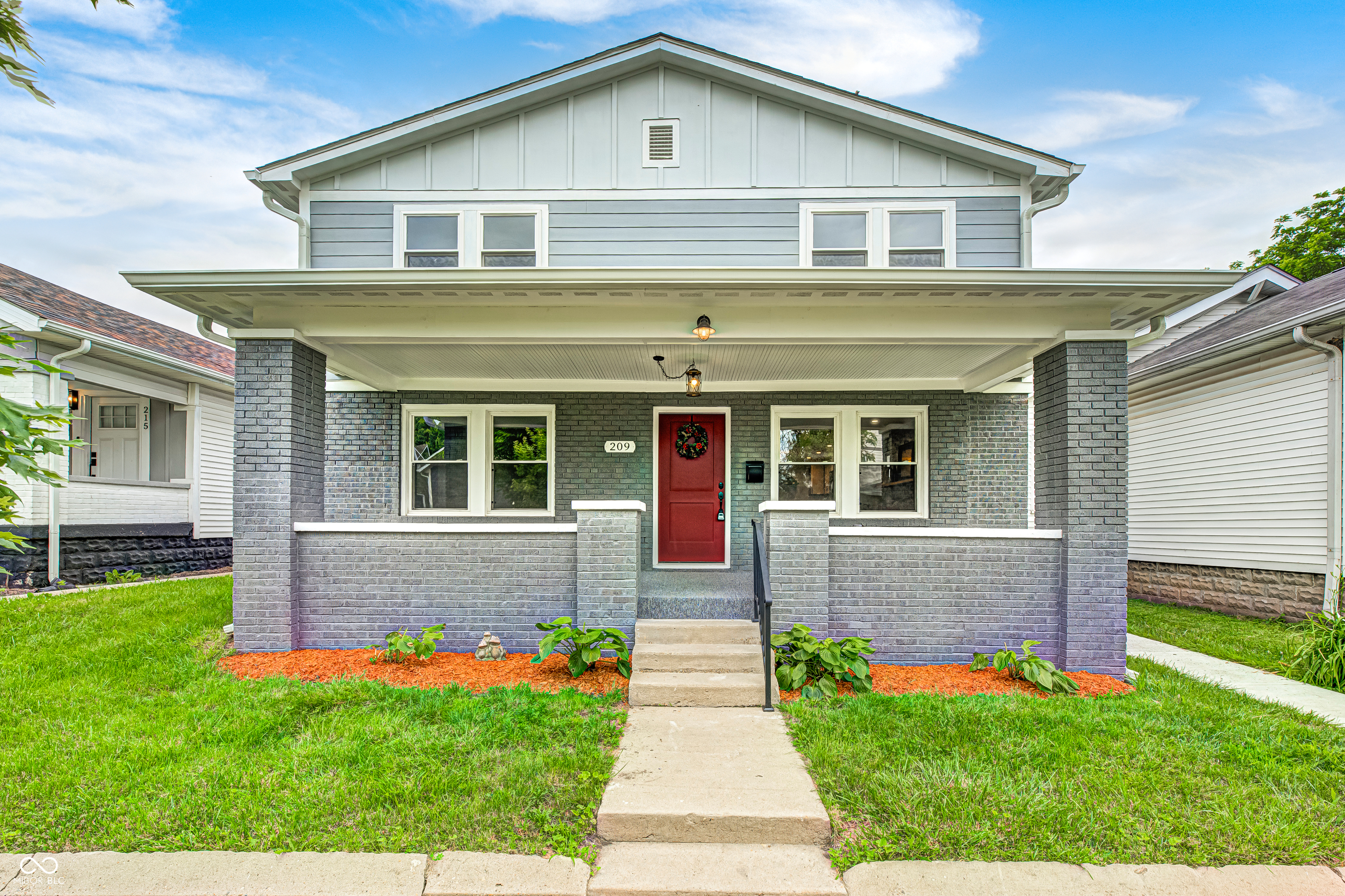 Two-story residence featuring a covered front porch, a red entry door, gray brick accents, and light gray siding