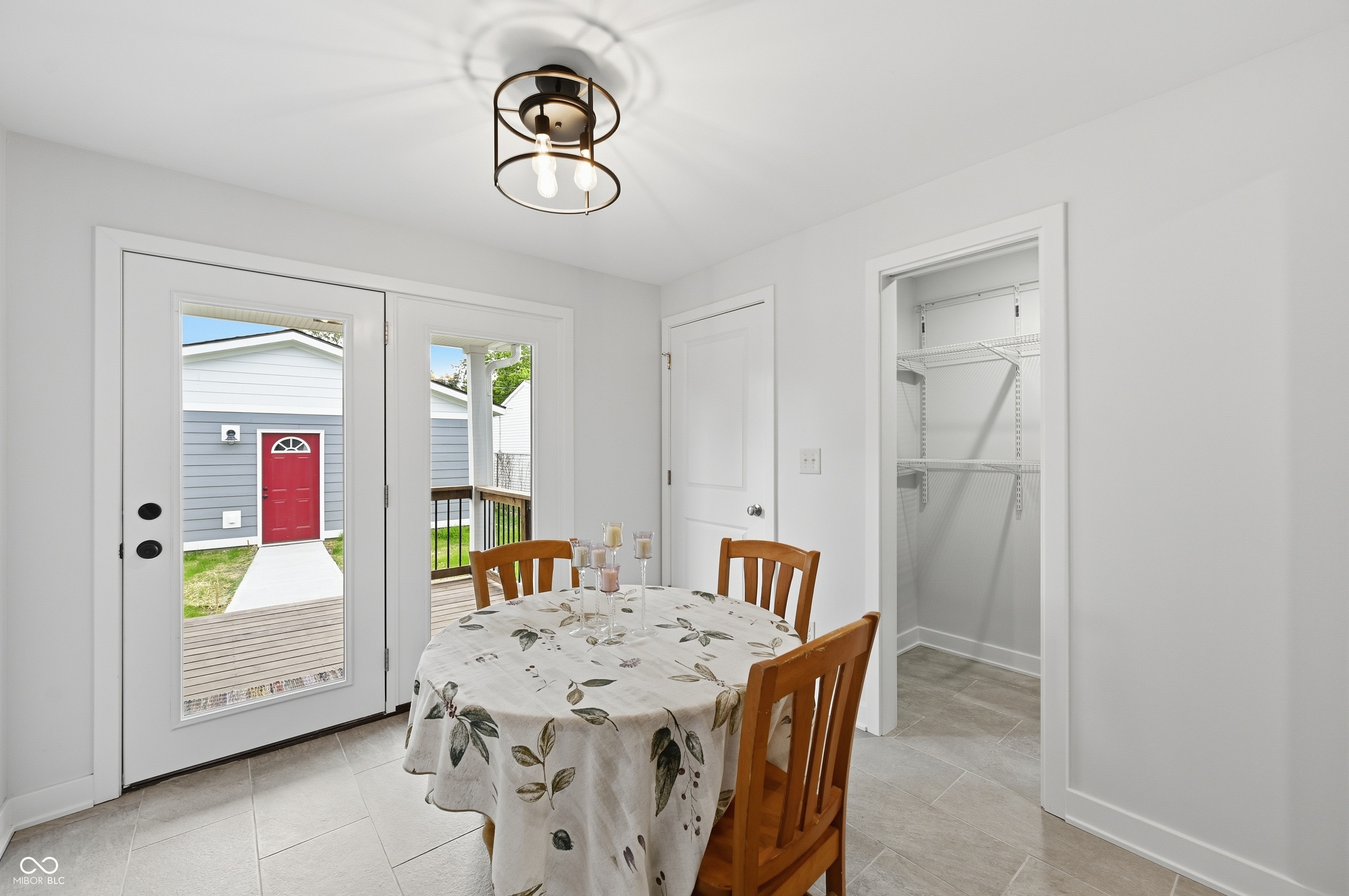Bright interior space featuring light-toned tile flooring, a contemporary black-framed ceiling light fixture, and white double French doors leading to an exterior deck