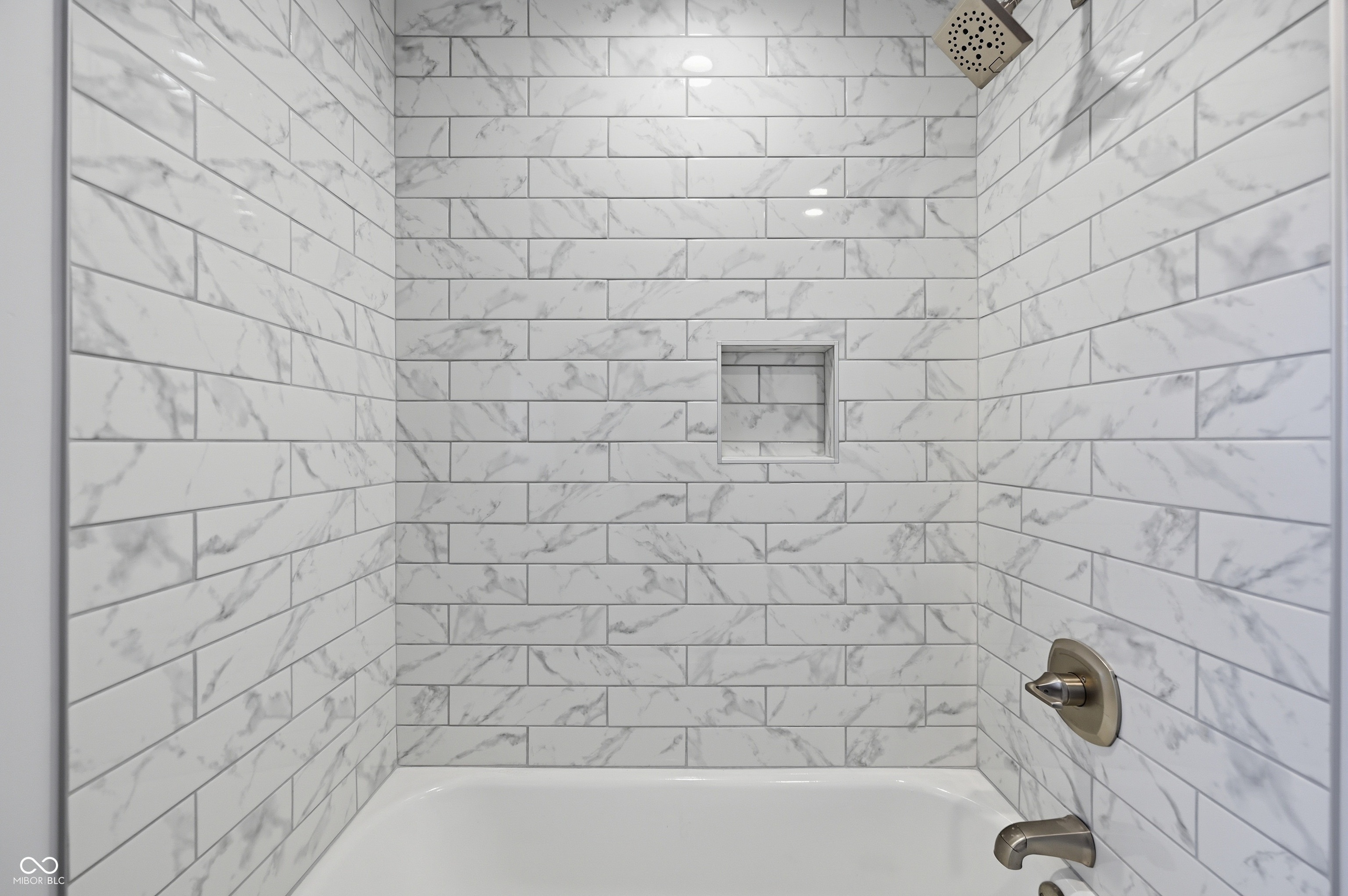 Bathtub shower combination featuring white subway tile surround with gray veining