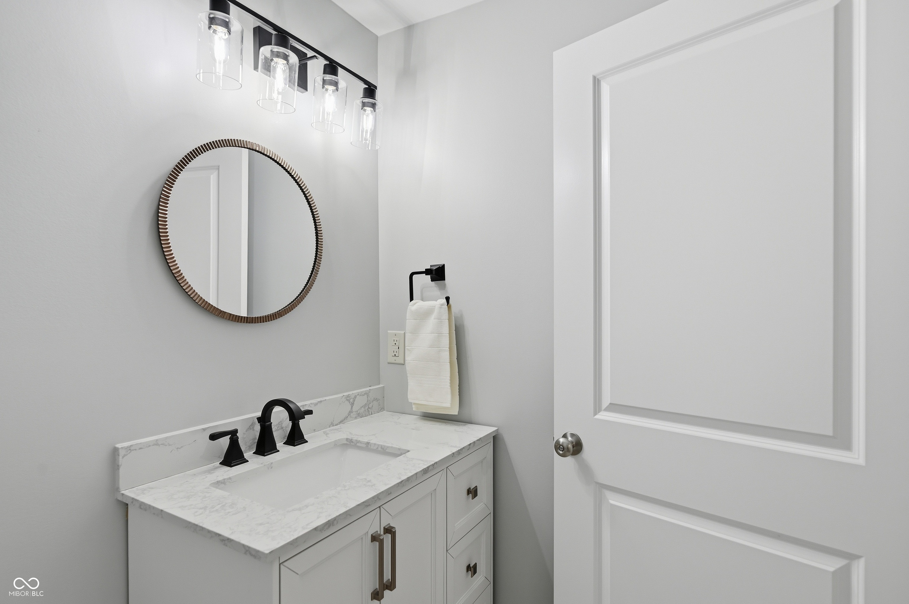Bathroom vanity featuring a white shaker-style cabinet with drawers and bronze hardware, topped with a stone-finish countertop and integrated rectangular sink