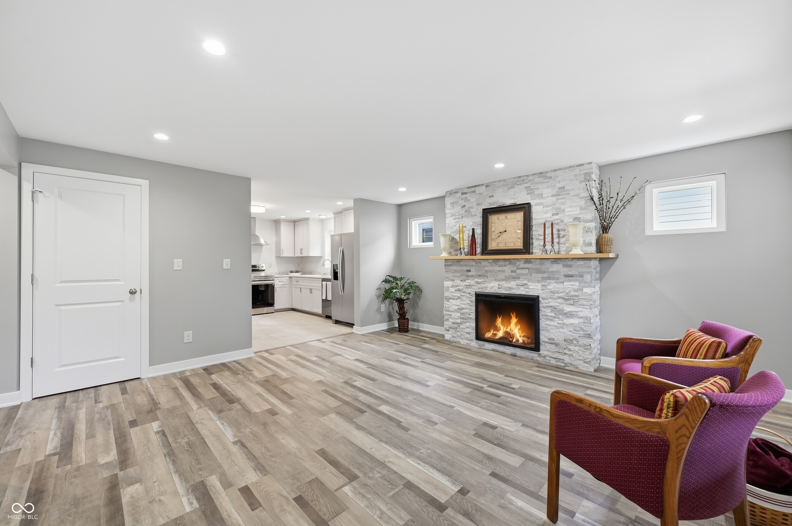 Living area featuring wood-finish flooring, recessed lighting, and a stone-clad fireplace with a light wood mantel Living area featuring wood-finish flooring, recessed lighting, and a stone-clad fireplace with a light wood mantel