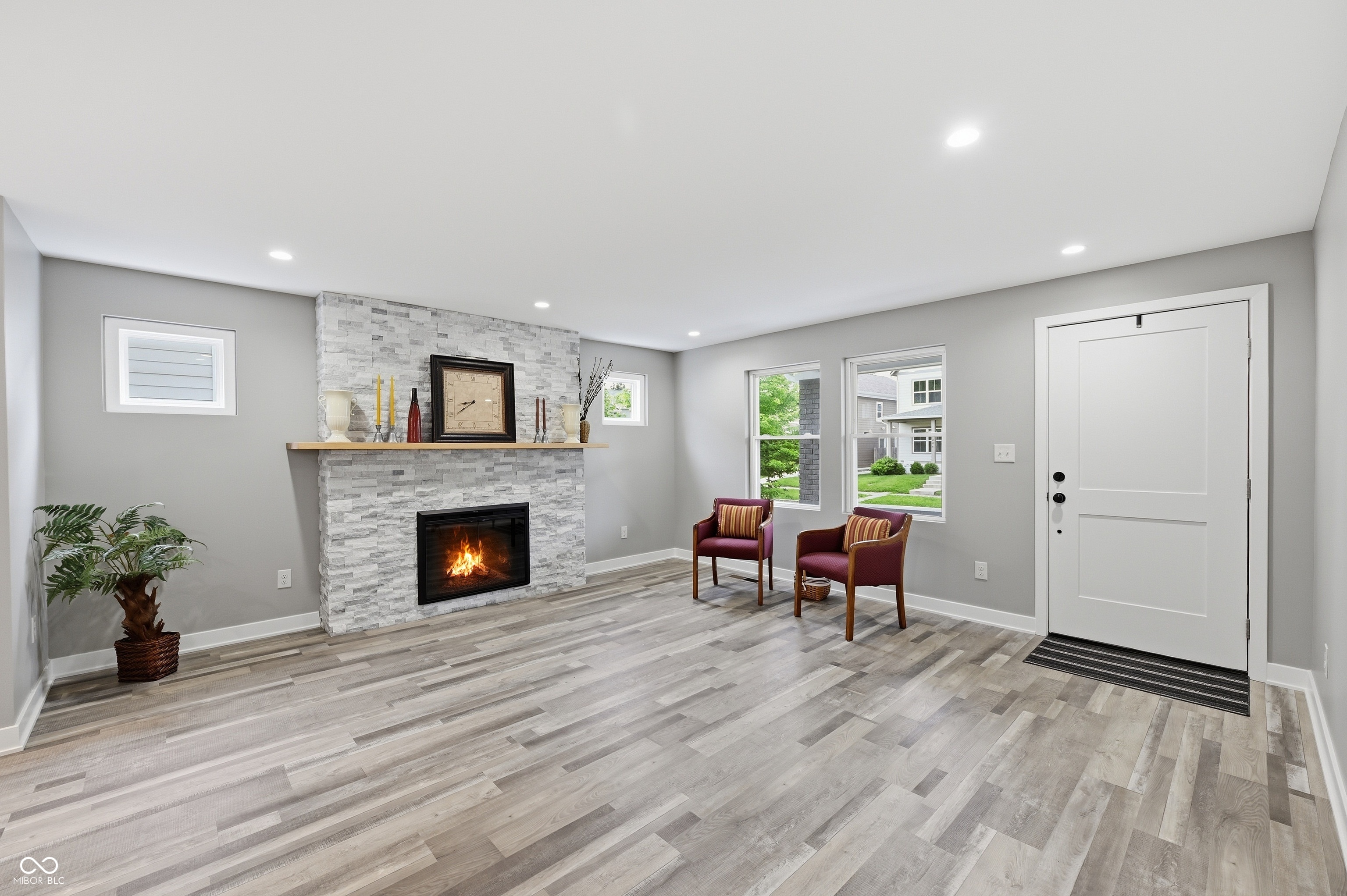 Spacious room featuring a stone-clad fireplace with a wood mantel, recessed lighting, and wood-finish flooring Spacious room featuring a stone-clad fireplace with a wood mantel, recessed lighting, and wood-finish flooring