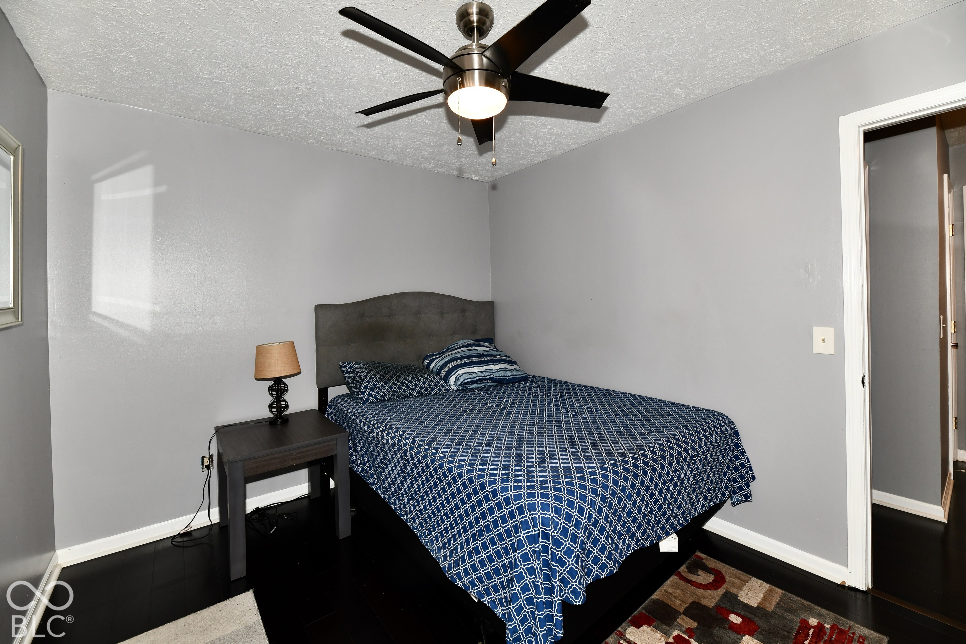 Neutral-toned walls featuring a ceiling-mounted fan with integrated lighting and dark-toned wood-finish flooring
