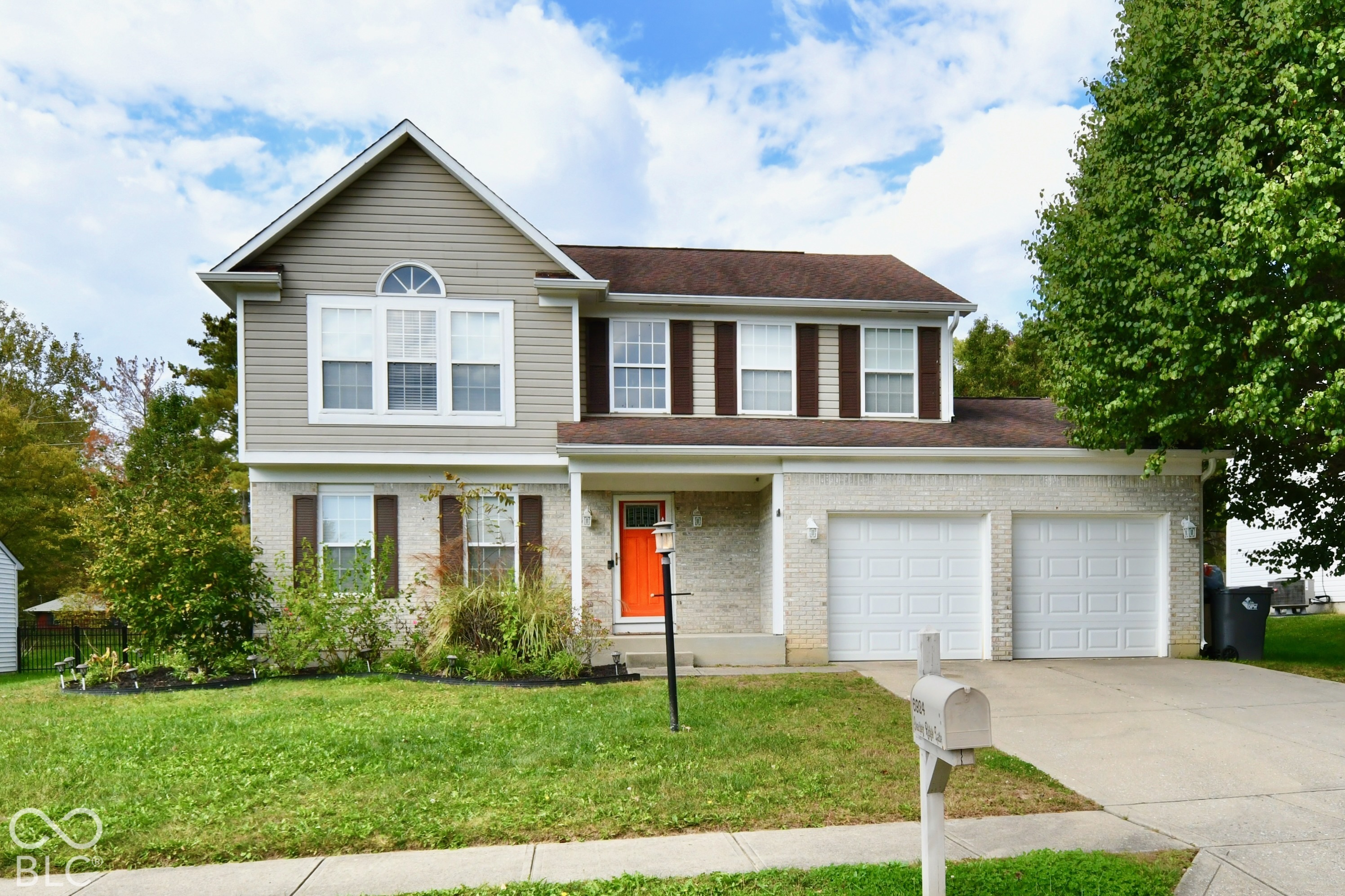 Two-story residence featuring light-colored brick and horizontal siding, an attached two-car garage, decorative window shutters, and a covered front entryway Two-story residence featuring light-colored brick and horizontal siding, an attached two-car garage, decorative window shutters, and a covered front entryway