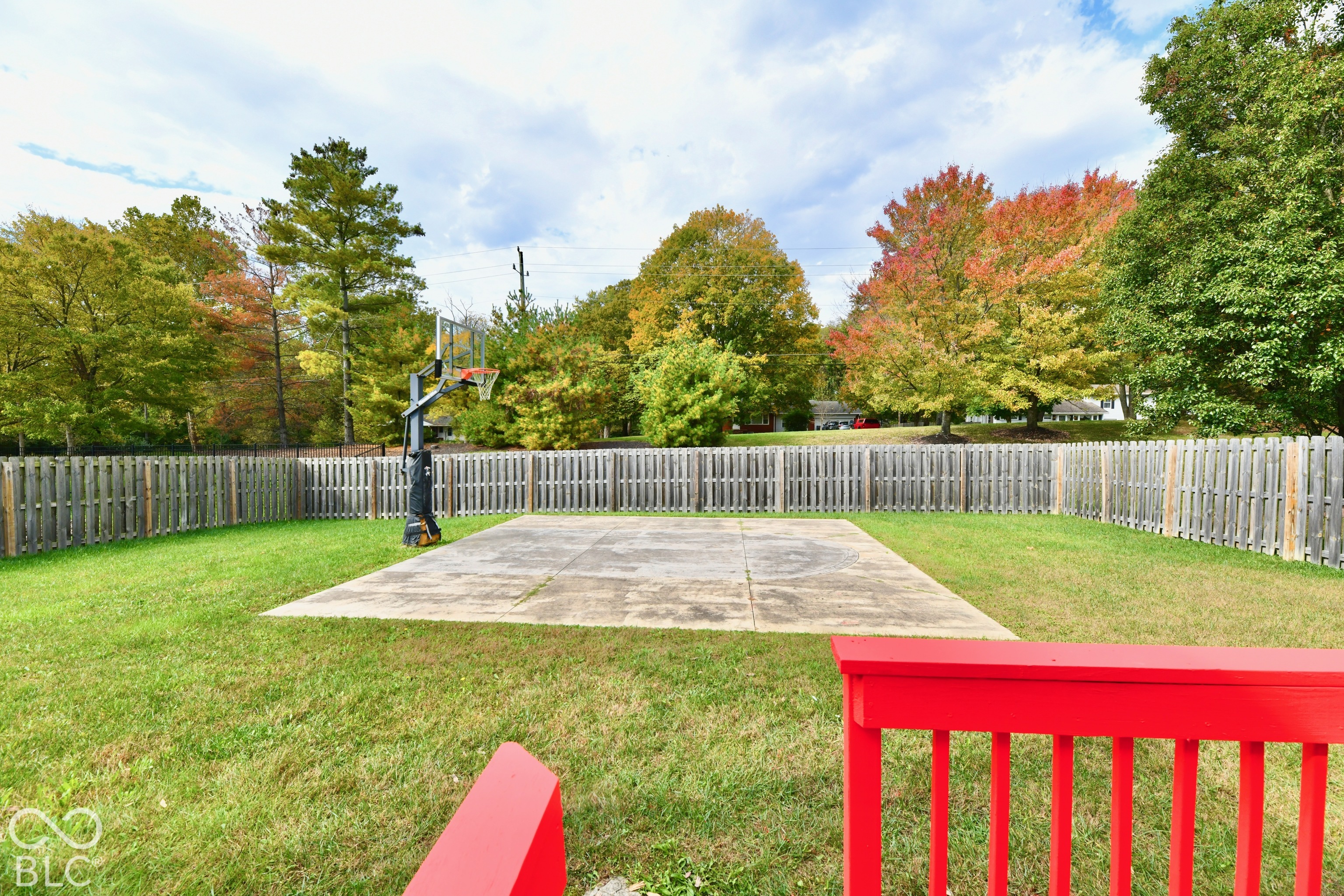Backyard featuring a concrete sport court, built-in basketball hoop, perimeter wood privacy fencing, and expansive grass lawn