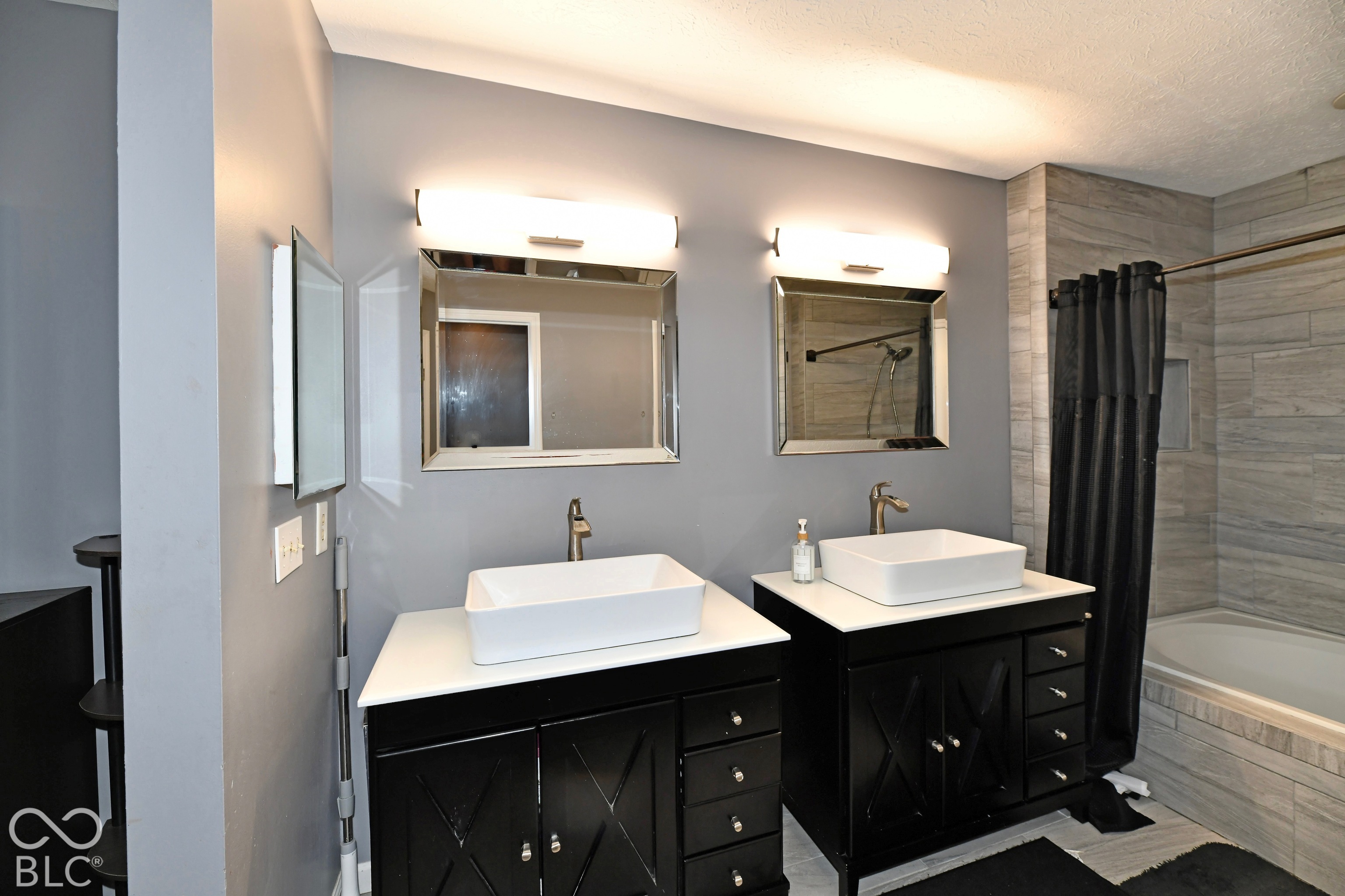 Dual vanity with matte black cabinetry, rectangular vessel sinks, light-toned countertops, and wall-mounted vanity lighting