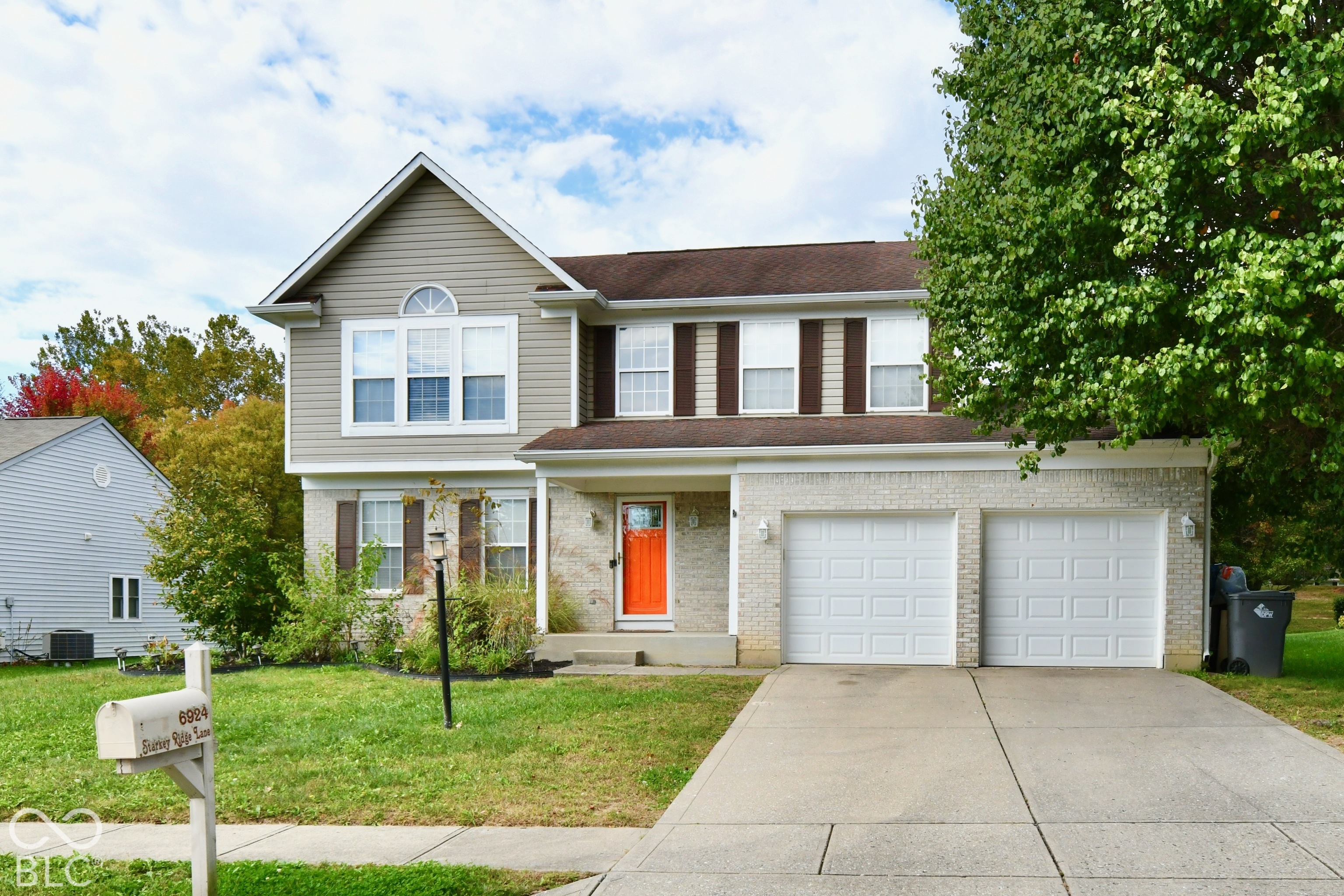 Two-story residence featuring a mixed-material facade of light-toned brick and horizontal siding, an attached two-car garage, and a covered front entryway Two-story residence featuring a mixed-material facade of light-toned brick and horizontal siding, an attached two-car garage, and a covered front entryway