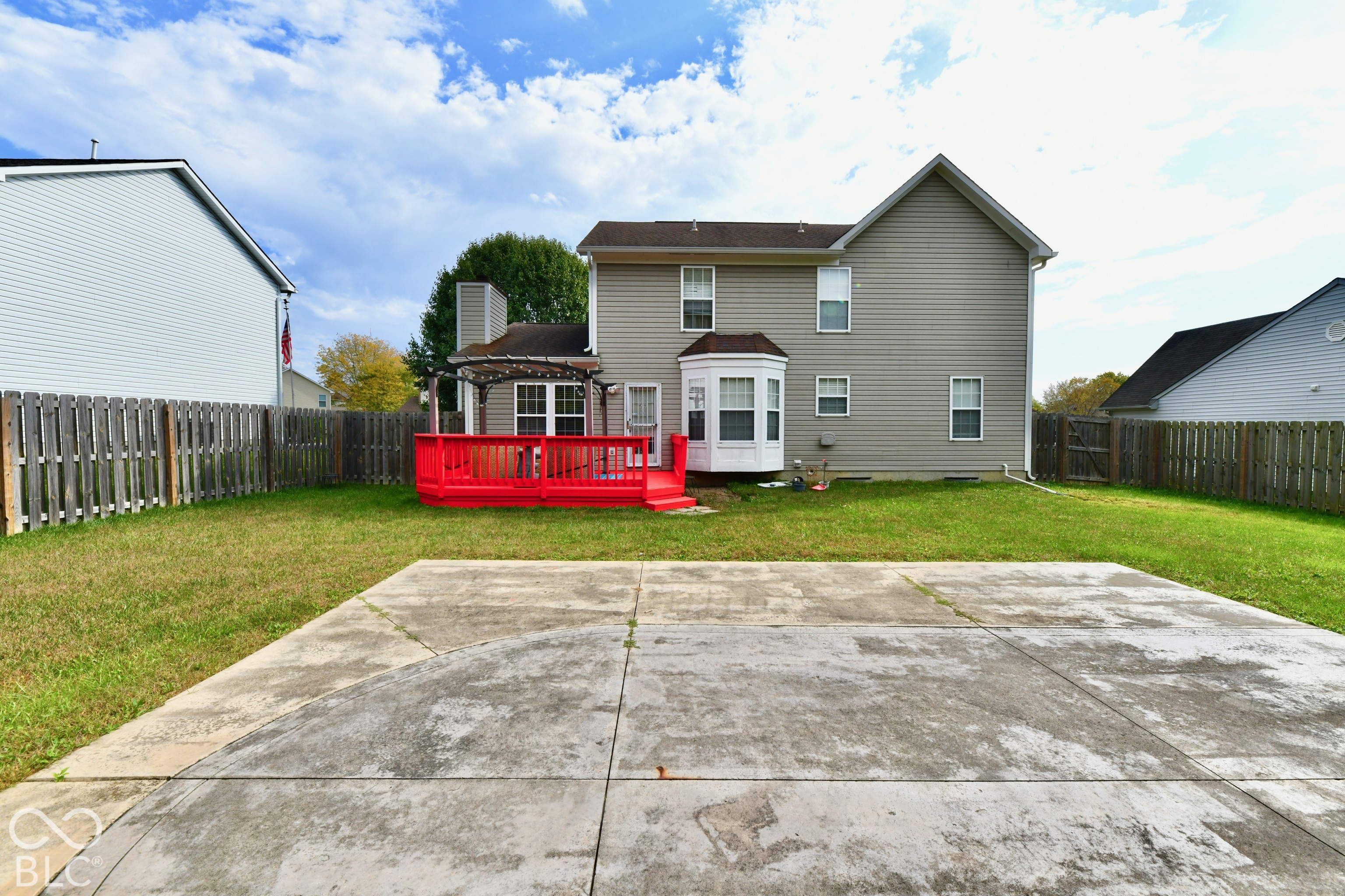 Rear exterior featuring a tiered wooden deck with an integrated pergola, concrete patio, bay window, and fenced backyard