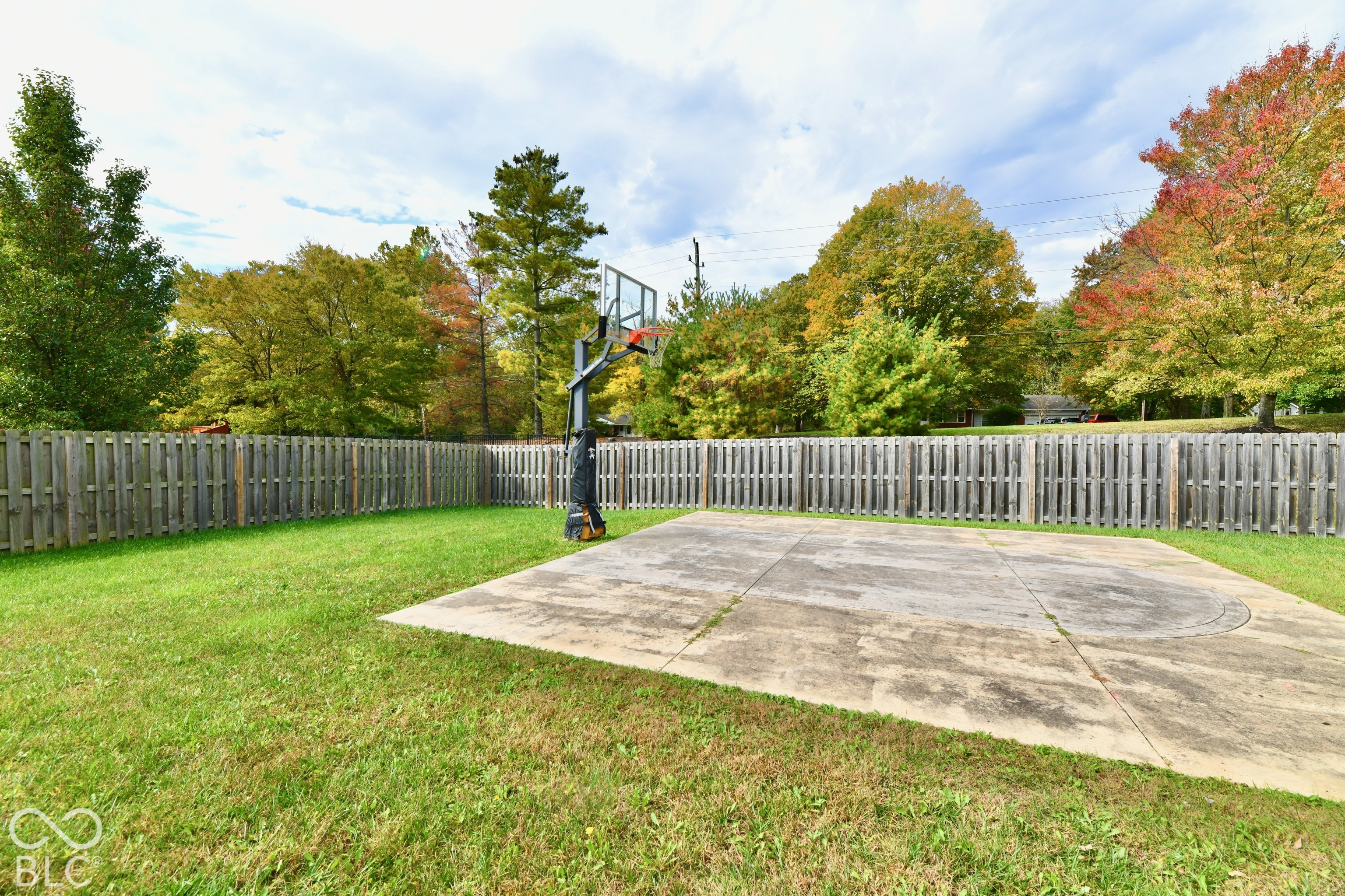 Fenced backyard featuring a concrete sports court and an attached basketball hoop