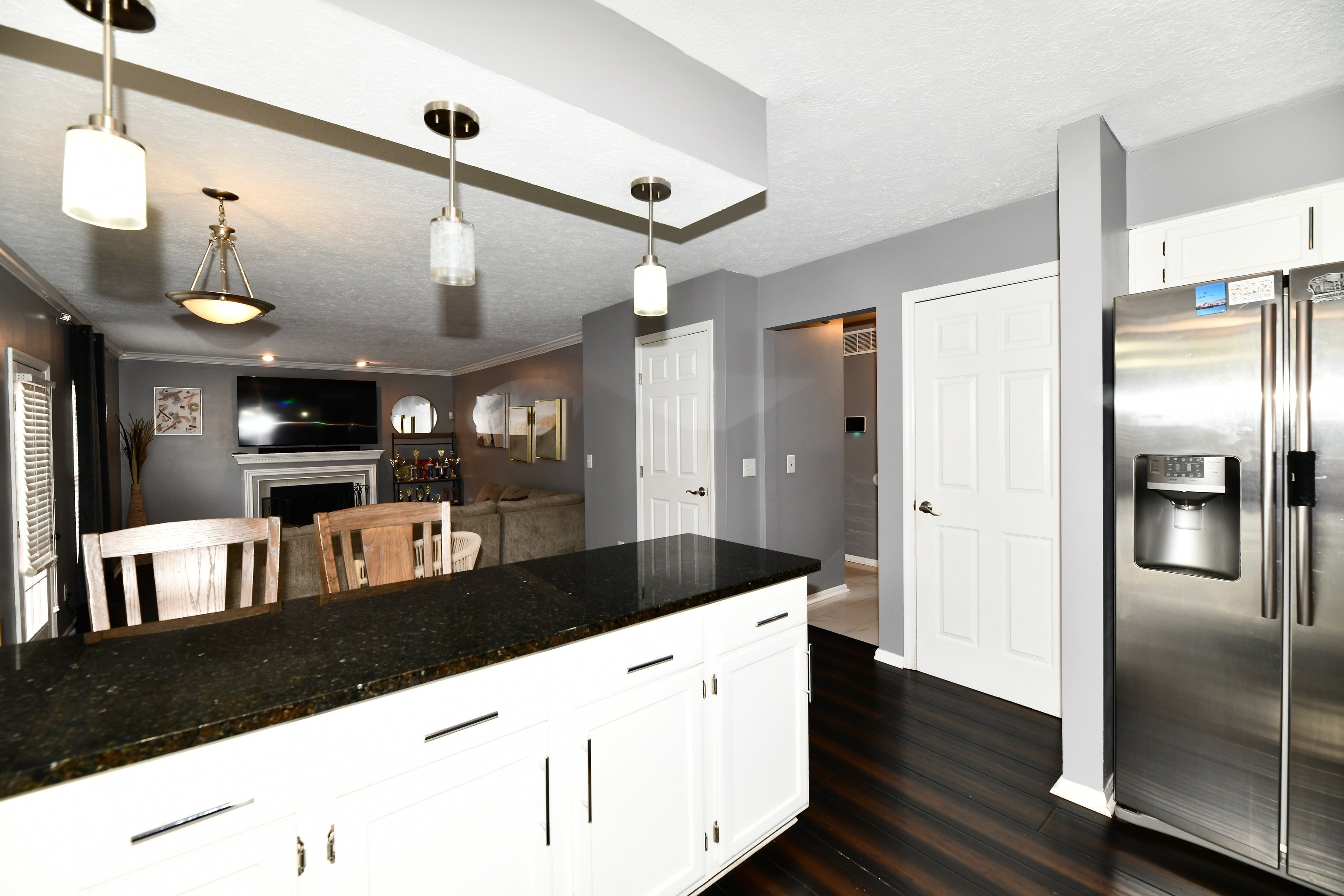 Kitchen island with dark stone countertop, white cabinetry, stainless steel side-by-side refrigerator, pendant lighting, and wood-finish flooring
