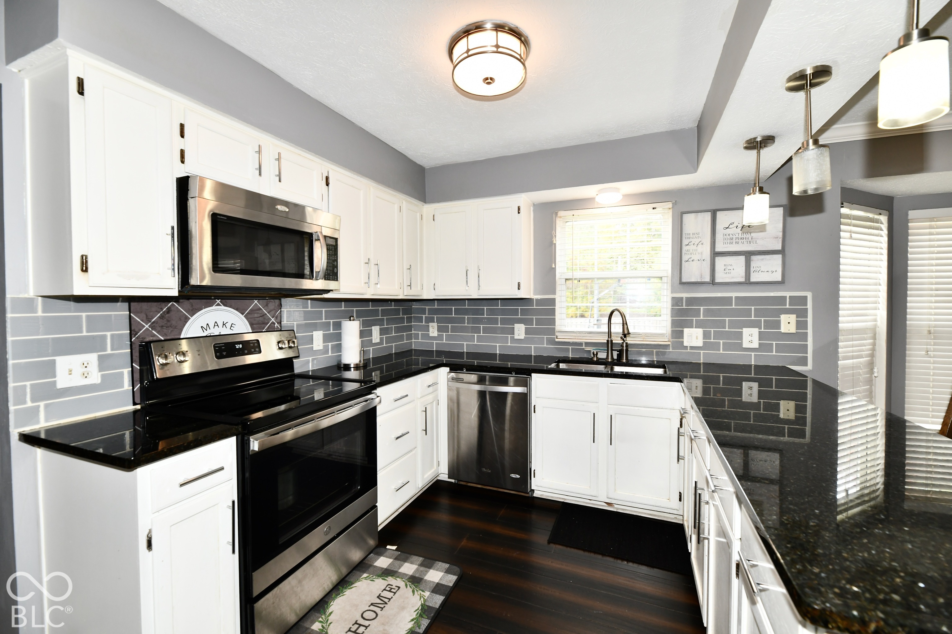 Kitchen featuring white shaker-style cabinetry, dark stone countertops, stainless steel appliances, grey subway tile backsplash, and dark wood-finish flooring