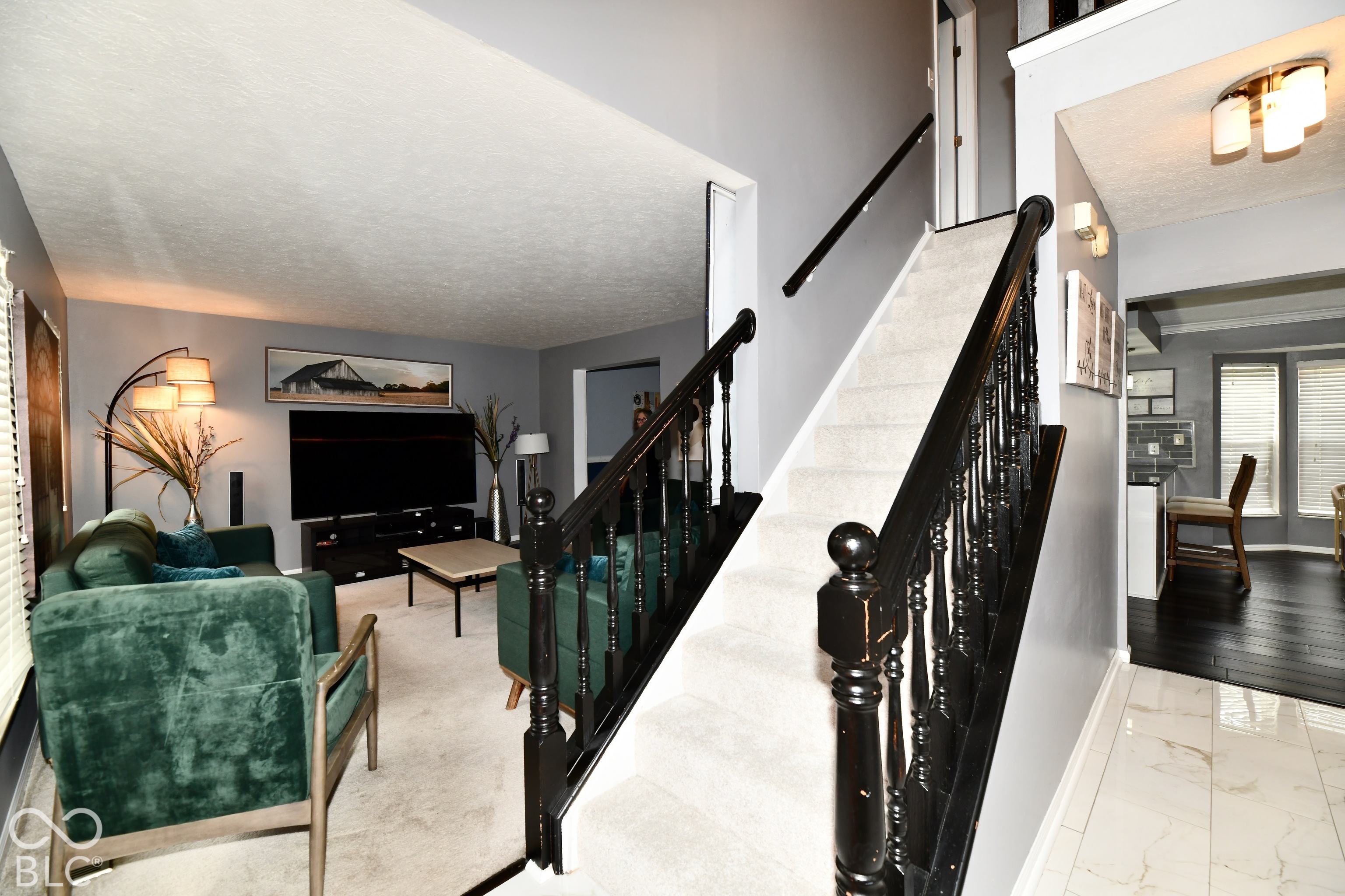 Open-concept interior featuring a staircase with black painted wood balusters and handrails, high-contrast wall finishes, polished tile flooring, and neutral carpeting