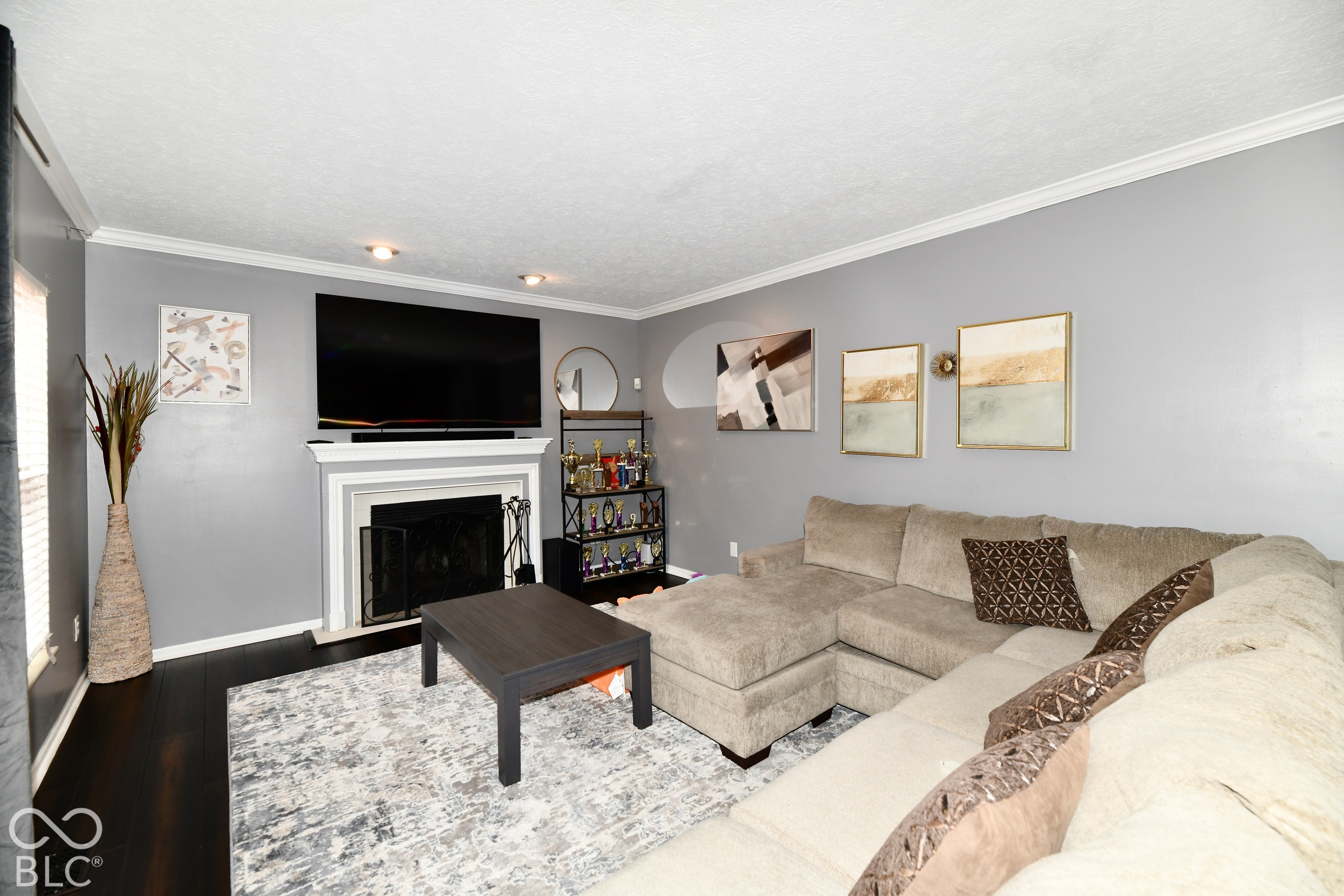 Living room featuring dark wood-finish flooring, crown molding, and a fireplace with a decorative mantel