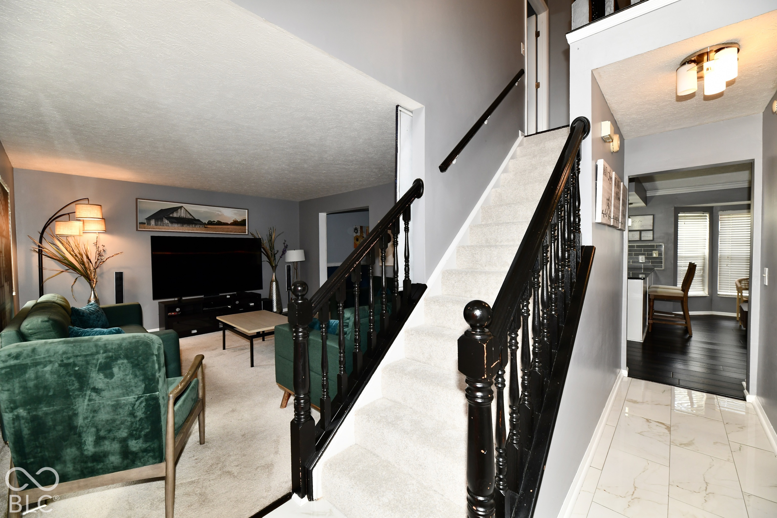Staircase featuring a black handrail and turned balusters with carpeted treads, stone-style tile flooring in the entry, and high ceilings