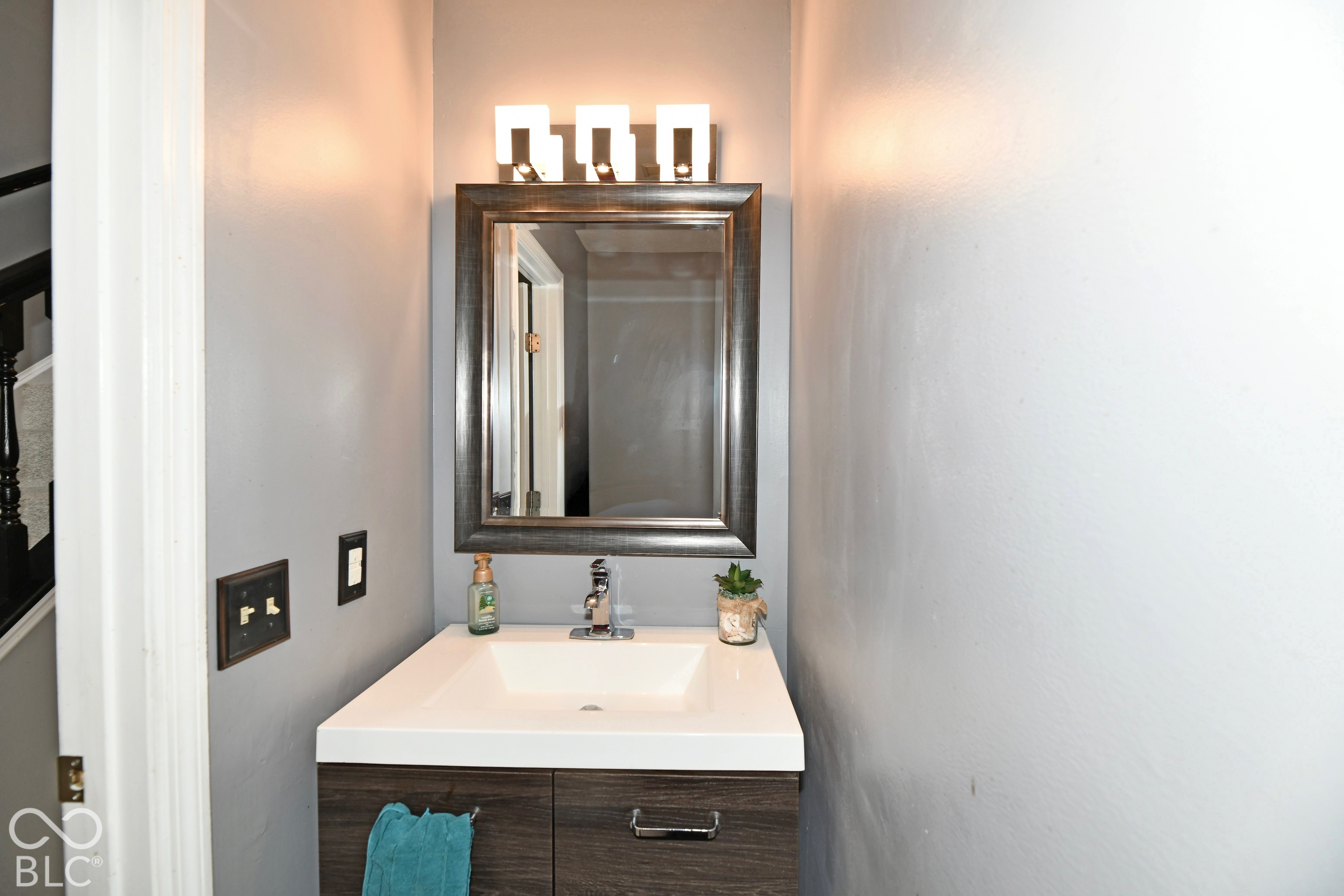 Modern vanity featuring a square vessel sink, dark wood-finish cabinetry, brushed metal hardware, and a three-light wall-mounted fixture with a rectangular mirror