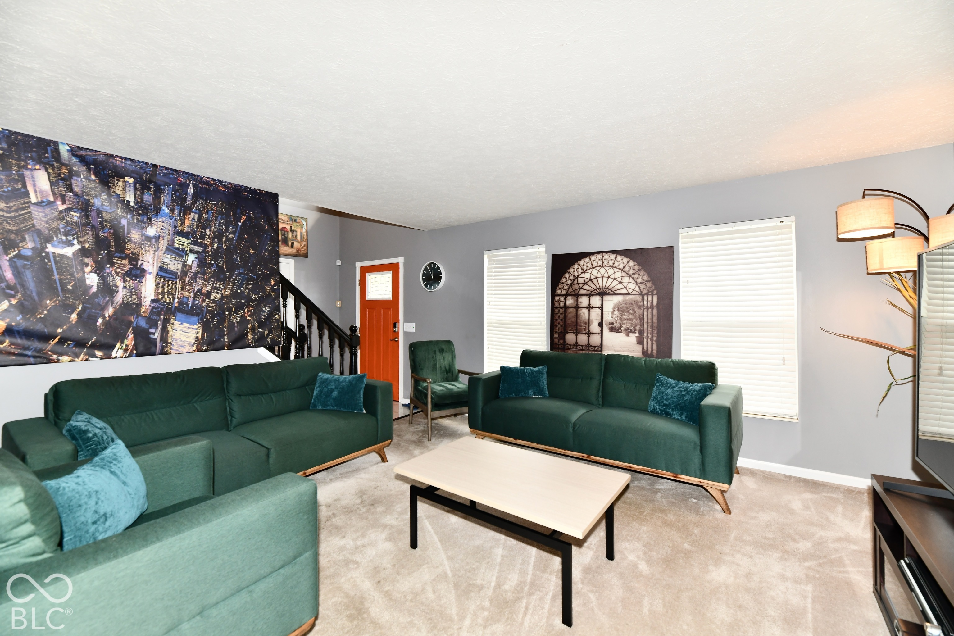 Living area featuring neutral carpeting, grey wall paint, two dual-pane windows with horizontal blinds, and a solid-core entry door with a glass inlay