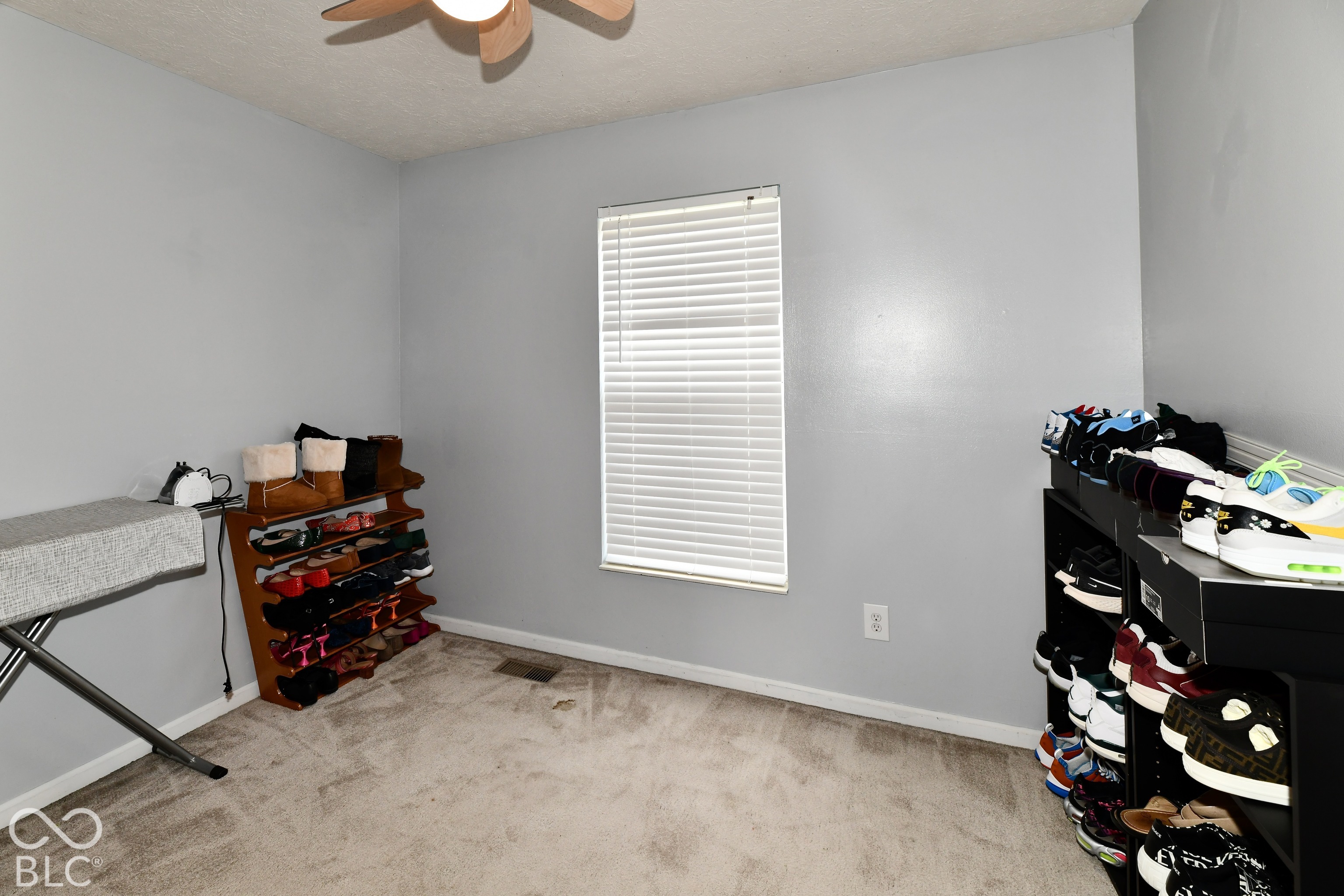 Neutral-toned interior room featuring wall-to-wall carpeting, a single window with horizontal blinds, and a ceiling-mounted light fixture