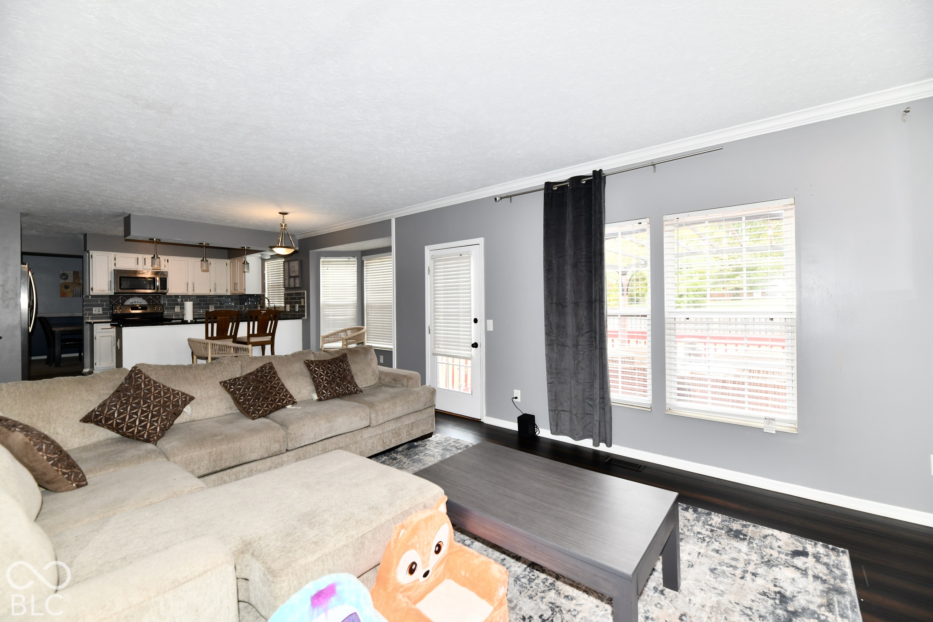 Living area featuring dark wood-finish flooring, neutral wall paint, and dual windows with fitted blinds