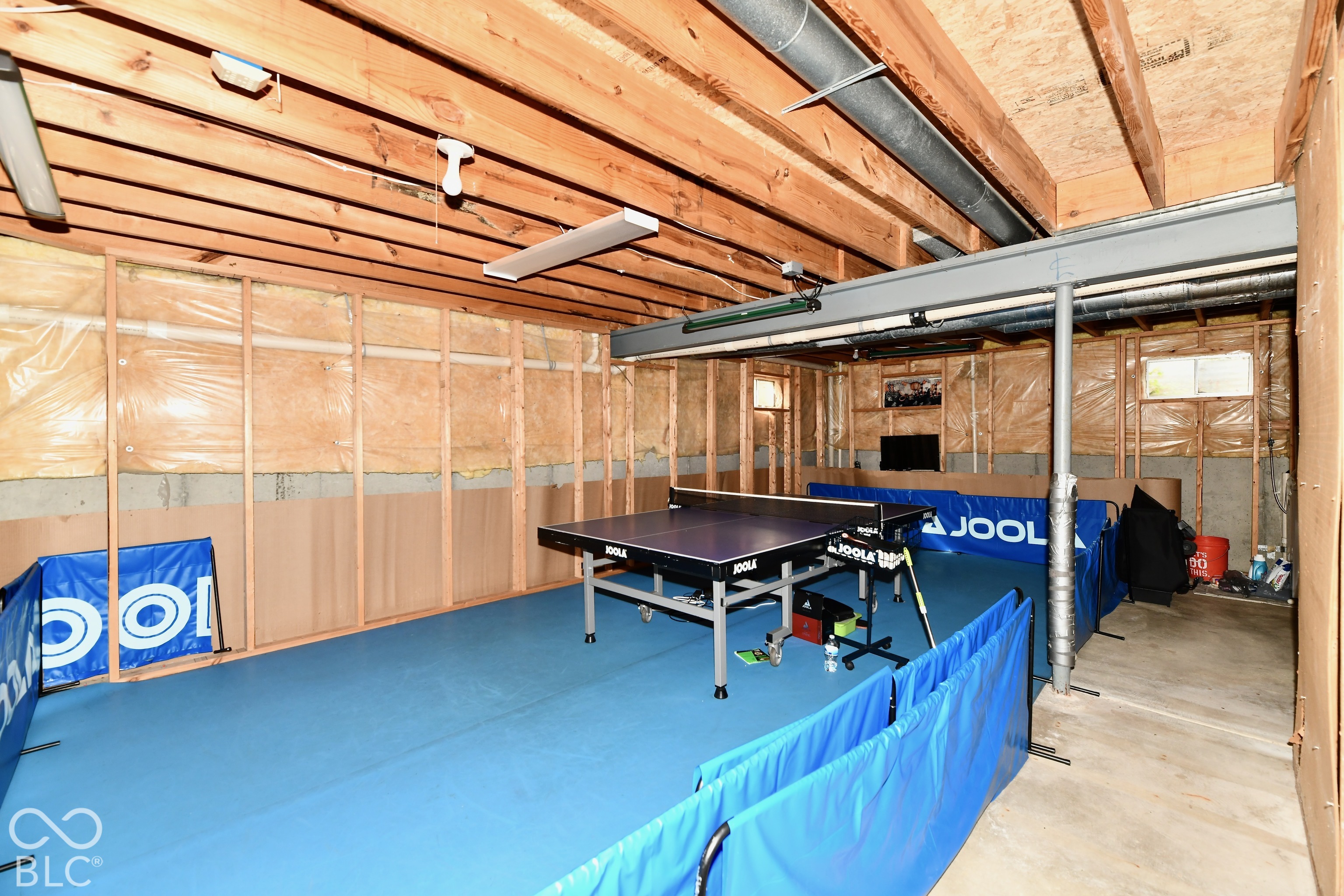 Unfinished lower level featuring exposed wood joist ceilings, concrete foundation walls, structural steel support beams, and utility lighting